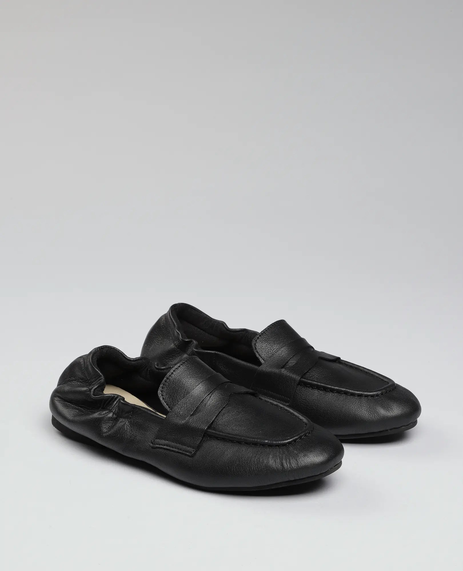 זוג נעלי מוקסין-נוריאל של B.unique בצבע שחור עם גב אלסטי, מוצגות על רקע אפור אחיד.