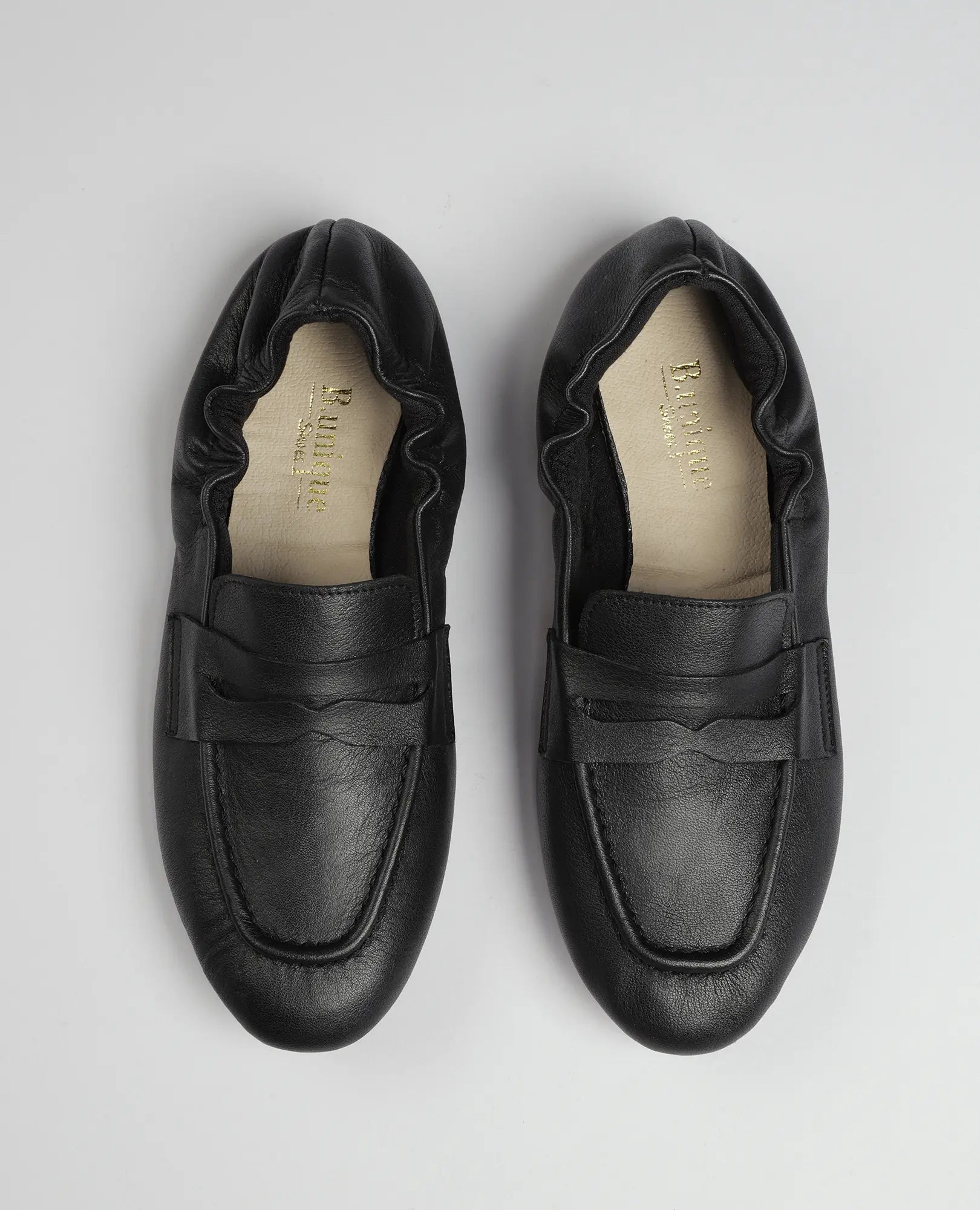 נעלי מוקסין-נוריאל מעור שחור בעיצוב עקב מקומט מבית B.unique, מוצגות על רקע אפור בהיר.