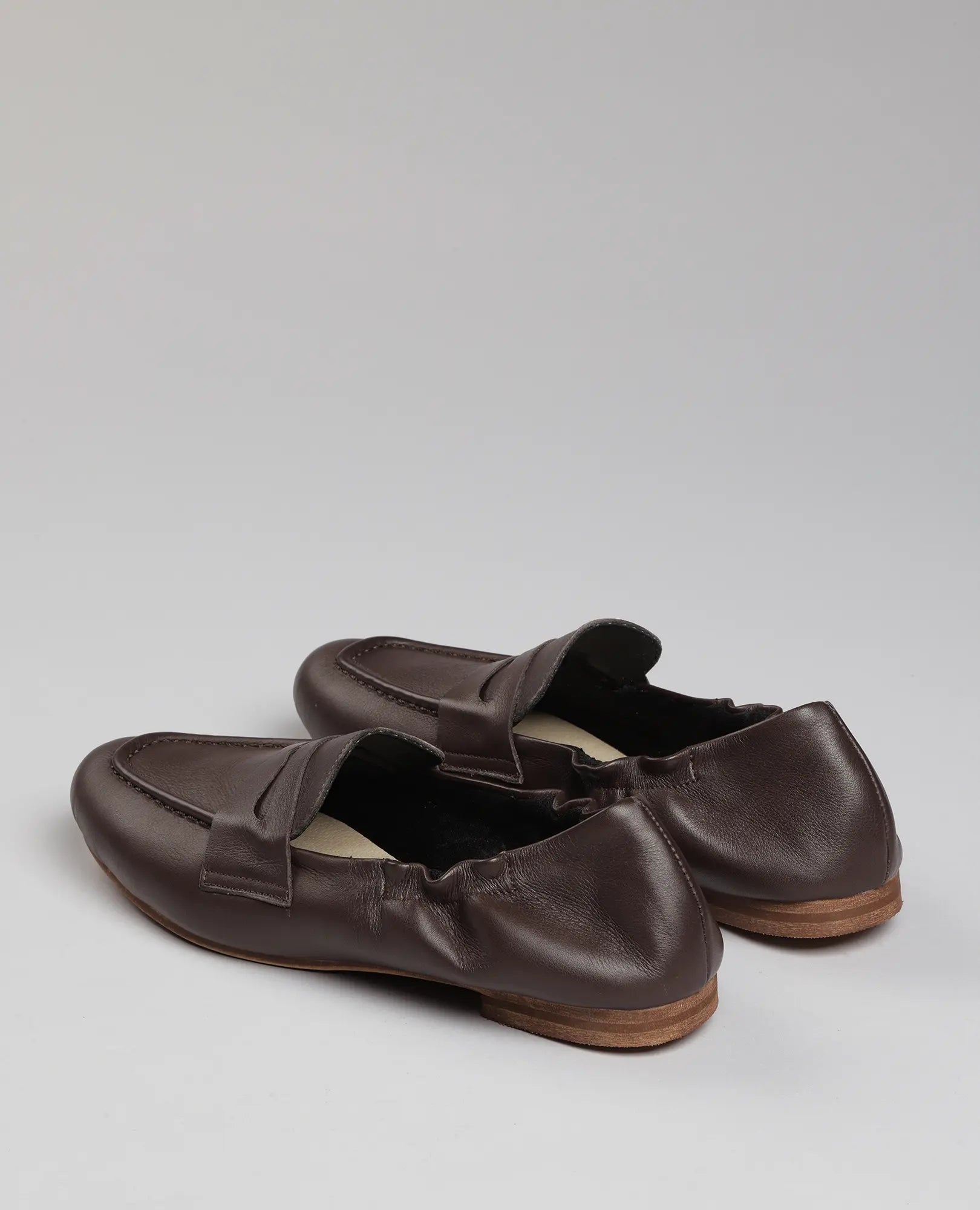 נעלי מוקסין-נוריאל מעור חומות עם סוליות עץ של B.unique, מוצגות באלגנטיות על רקע אפור בהיר.