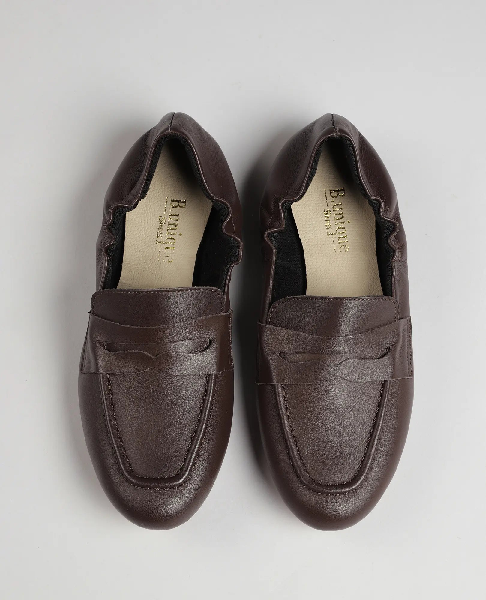 זוג נעלי מוקסין-נוריאל חומות של B.unique עם קפלים בצדדים, מוצגות מלמעלה על רקע אפור בהיר.