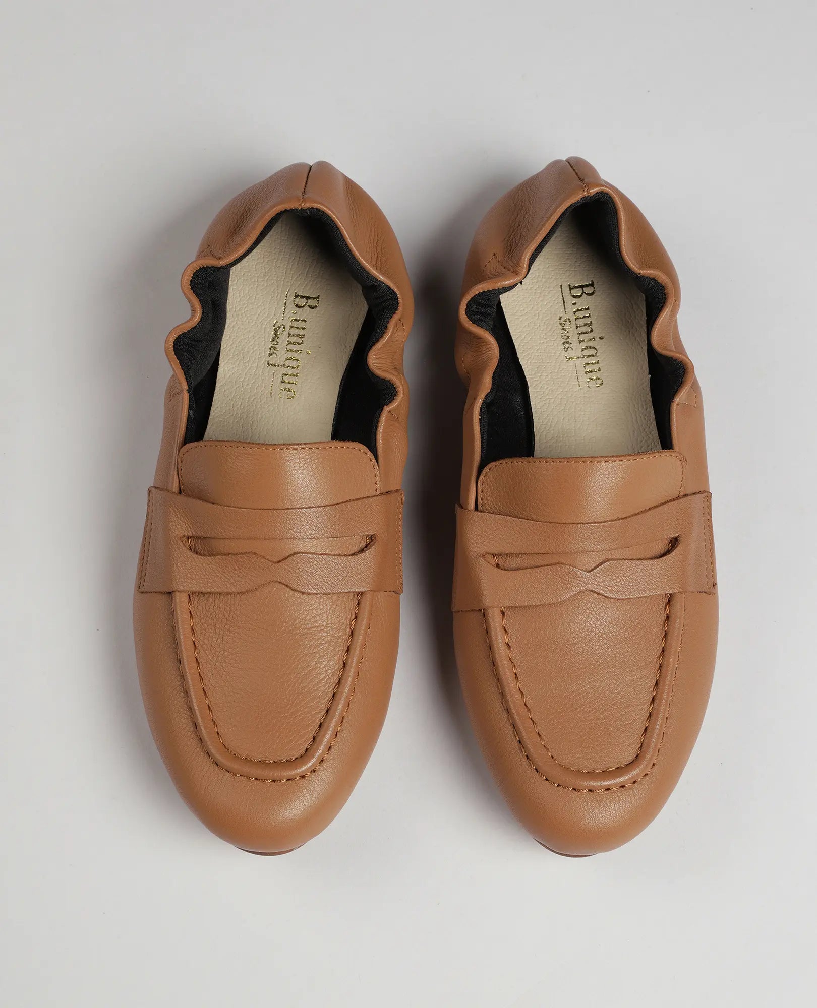 זוג נעלי מוקסין-נוריאל מעור בצבע חום בהיר של B.unique, עם קצוות מסולסלים, מוצגות מלמעלה על רקע בהיר.