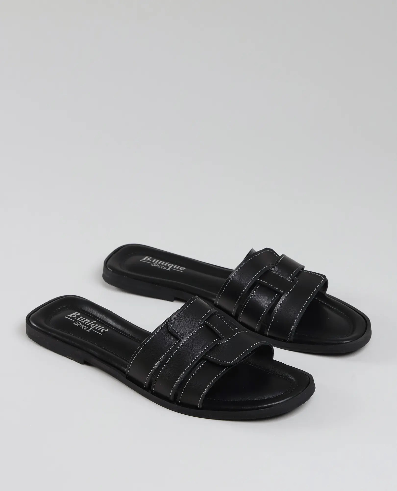 כפכפי רצועות סקיי שחורים של B.unique, עשויים מעור איכותי עם תפרים לבנים, על רקע בהיר ונקי.
