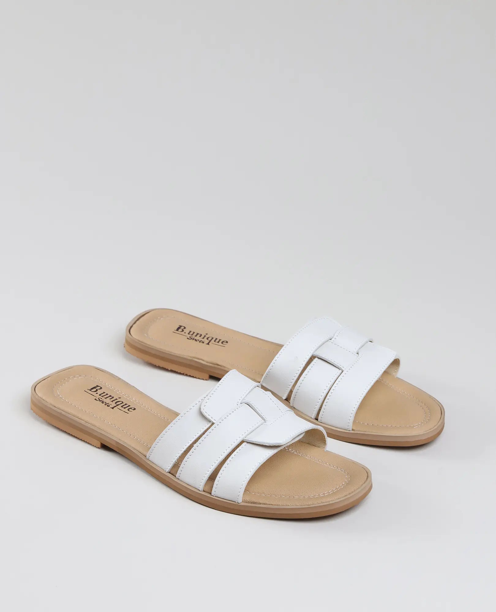 כפכפי רצועות-סקאיי של B.unique בצבע לבן, שטוחות עם סוליה בצבע חום בהיר ושתי רצועות, מעור איכותי.