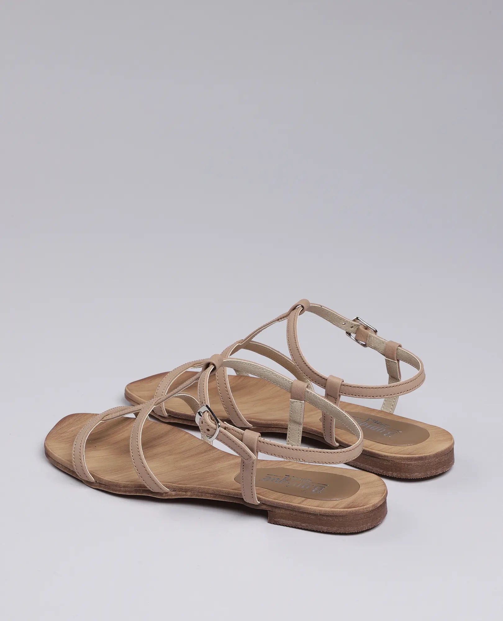 סנדלי גלדיאטור-קיילי מבית B.unique: סנדלים שטוחים בצבע בז' עם רצועות ואבזמים, על רקע בהיר.