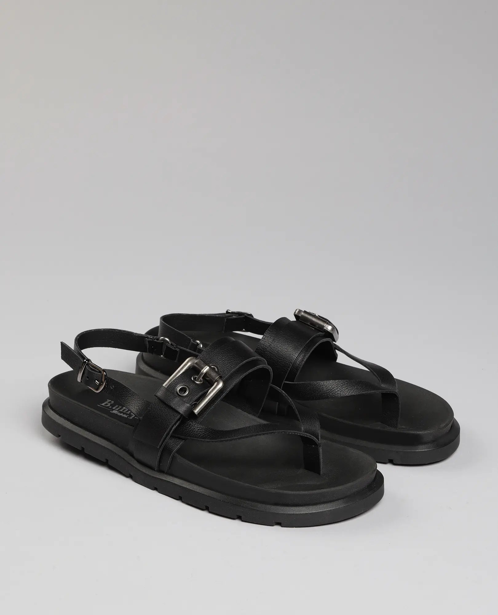 זוג סנדלי אצבע-פואט מבית B.unique, מעור שחור עם רצועות עבות, אבזמים ורצועת עקב על רקע חלק.