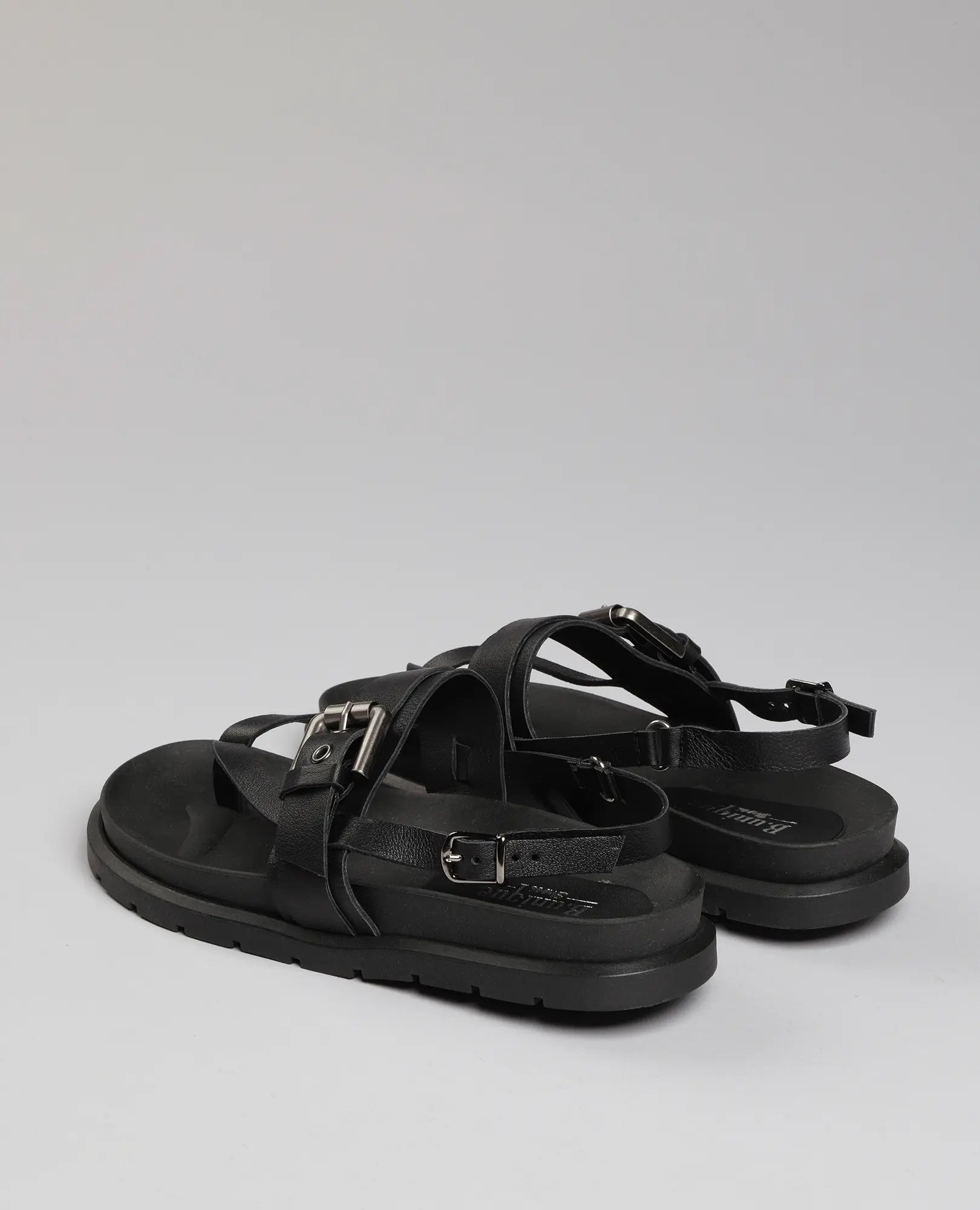 זוג סנדלי אצבע שחורים של B.unique מדגם "פואט", עם רצועות ואבזמים על רקע אפור בהיר.