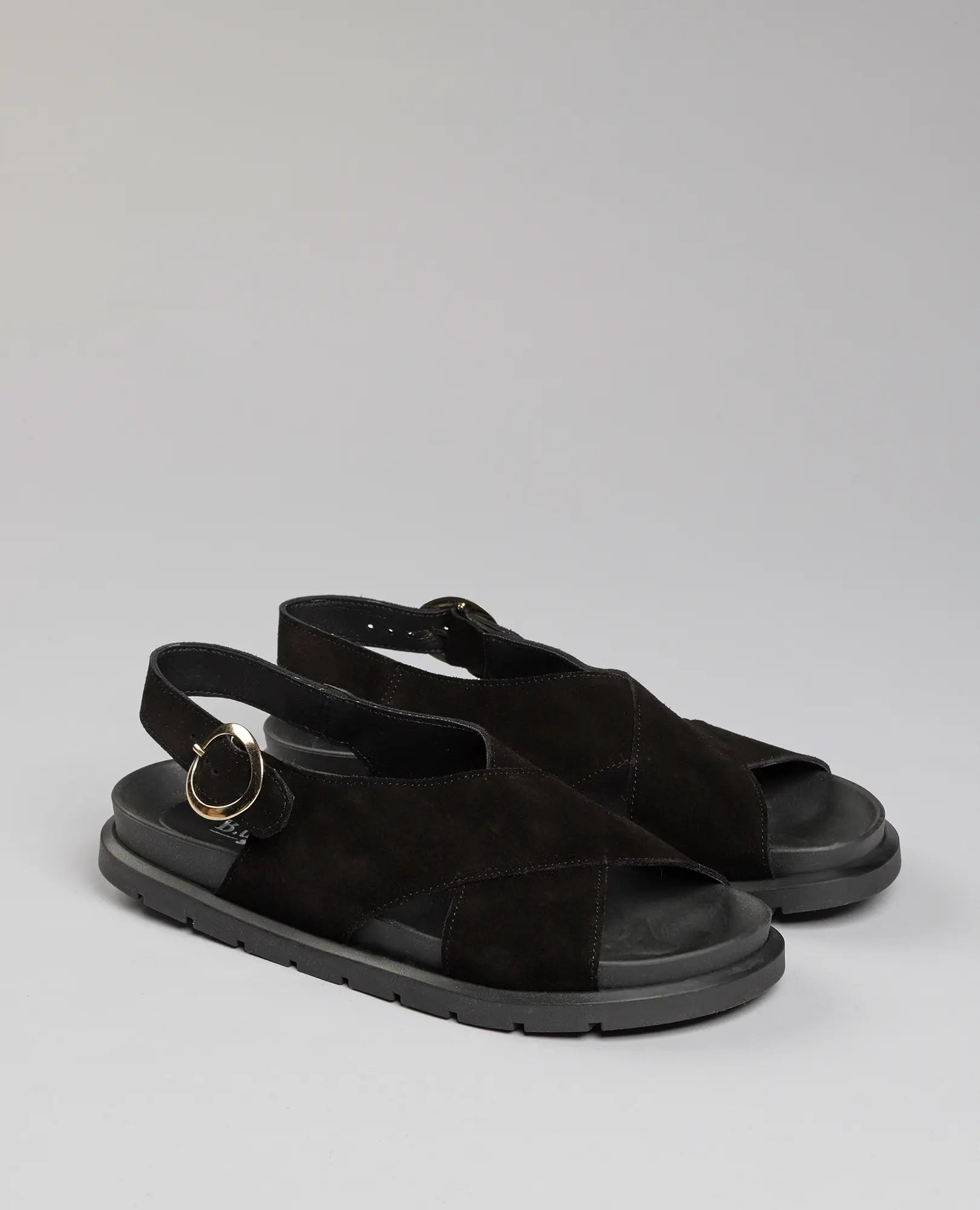 זוג סנדלים שטוחים מדגם "לוני" של המותג B.unique בצבע שחור, עם רצועות מצטלבות, אצבעות פתוחות ואבזמים כסופים, מוצג לראווה.