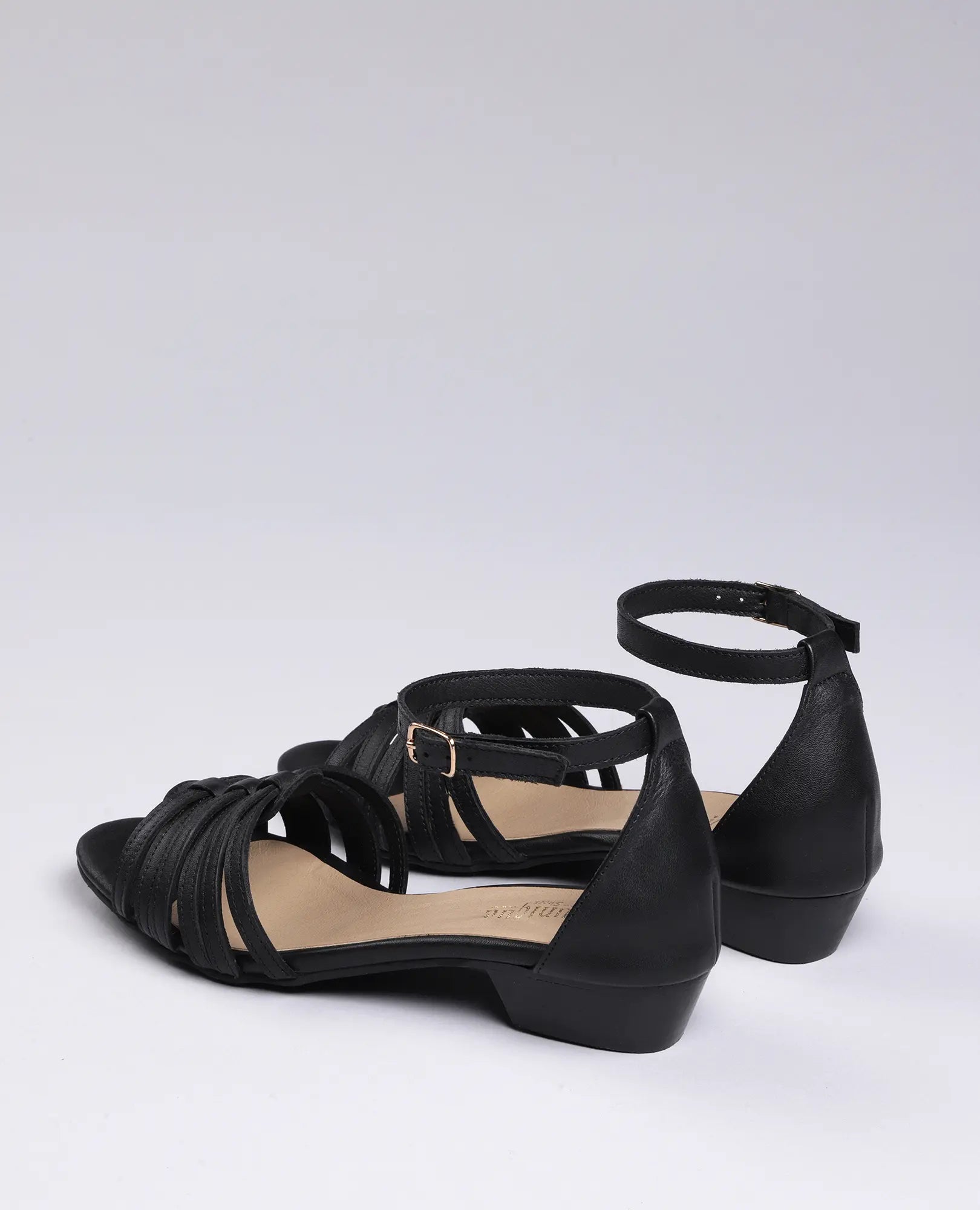 זוג סנדלי רצועות דקות בצבע שחור של המותג B.unique, עם עקב נמוך, מוצגים על רקע בהיר אחיד.