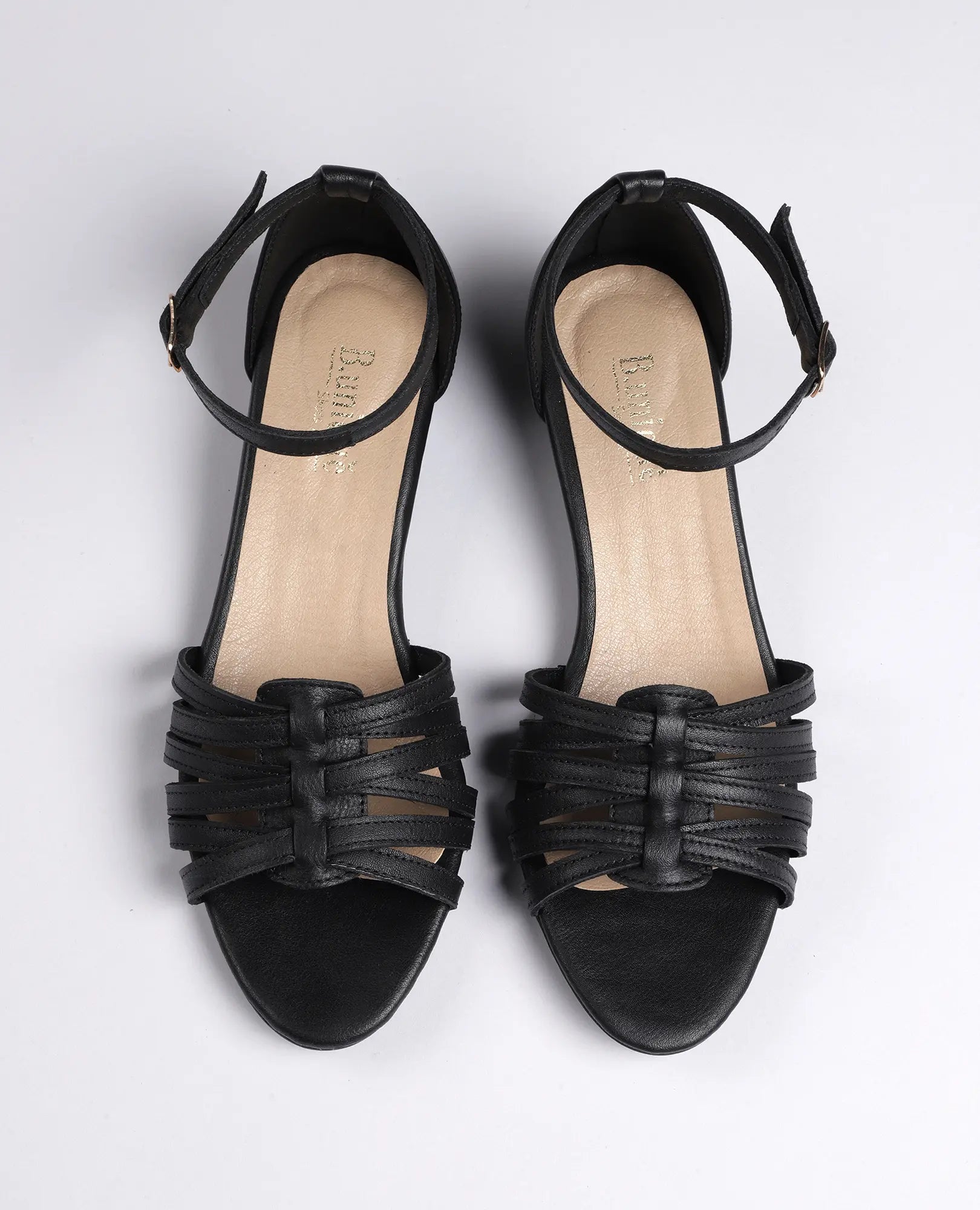 זוג סנדלי רצועות דקות מדגם "לוריה" של B.unique בצבע שחור, עם רצועות בקרסול ופרטים ארוגים על רקע לבן.