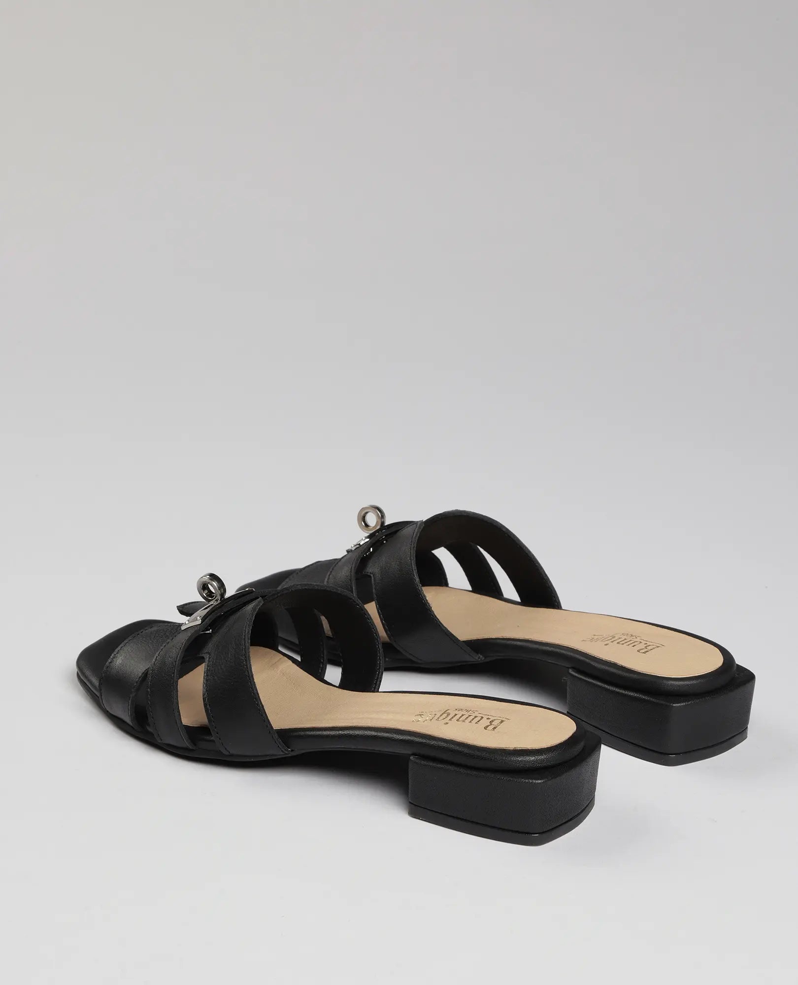 כפכפי רצועות עם אבזם – דגם "נעה" של B.unique: כפכפי עור שחורים עם עקב נמוך, רצועות צולבות רחבות וסוליה קלה.