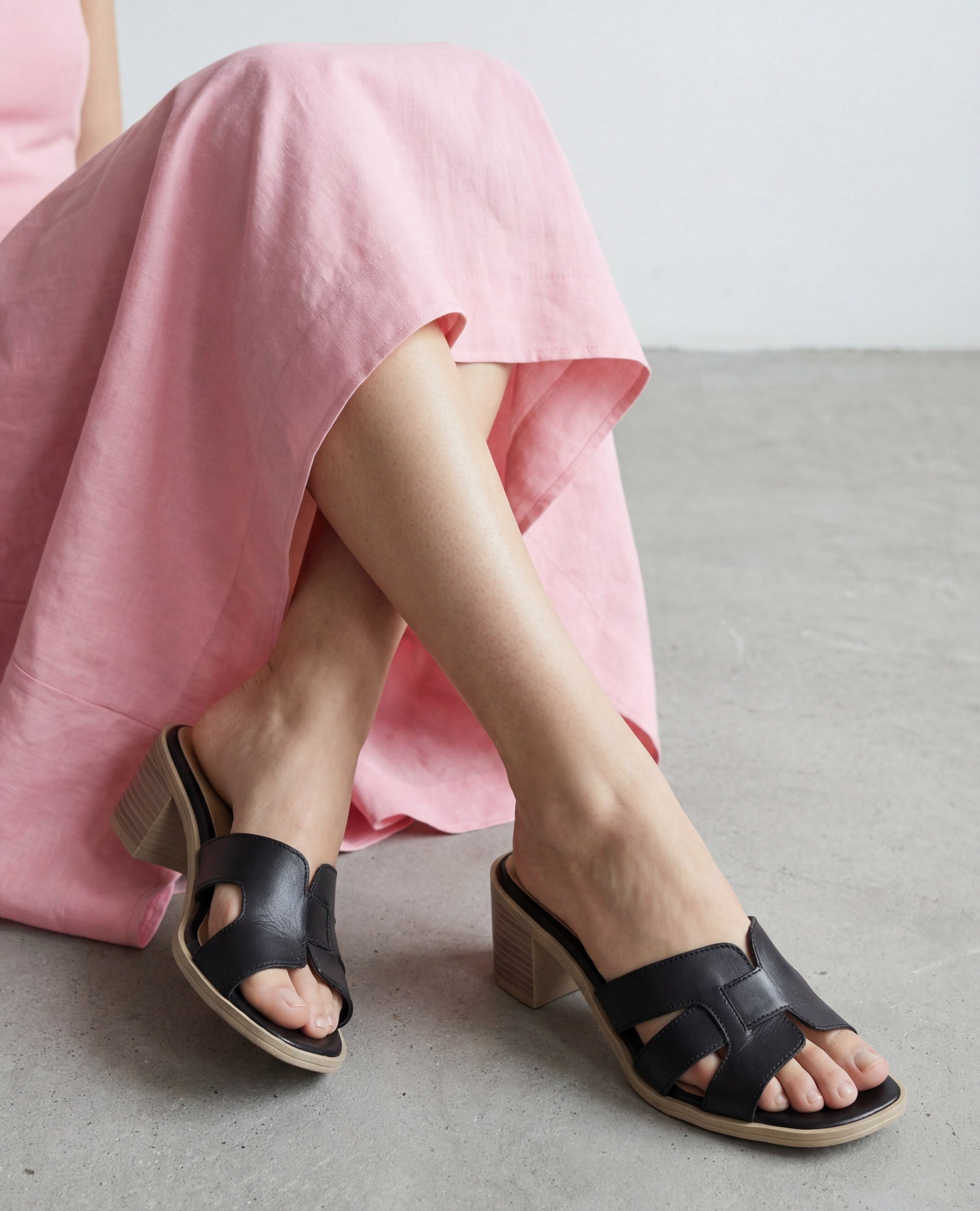 אישה בשמלה ורודה יושבת על הרצפה, נועלת כפכפי עקב - ניבר בצבע שחור של B.unique.