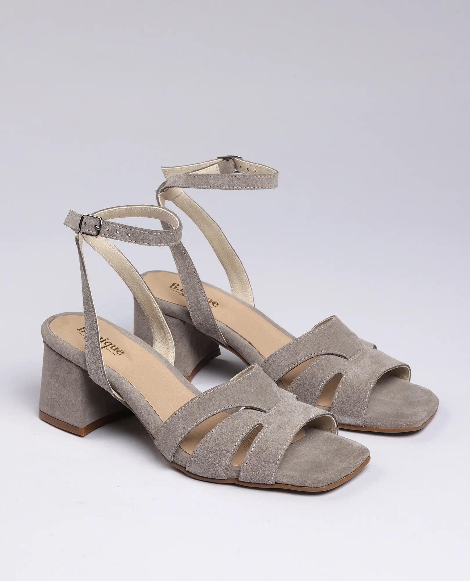סנדלי עקב "ארבל" של B.unique מעור זמש אפור בהיר עם רצועת קרסול ועקב בלוק, מוצגים על רקע חלק.