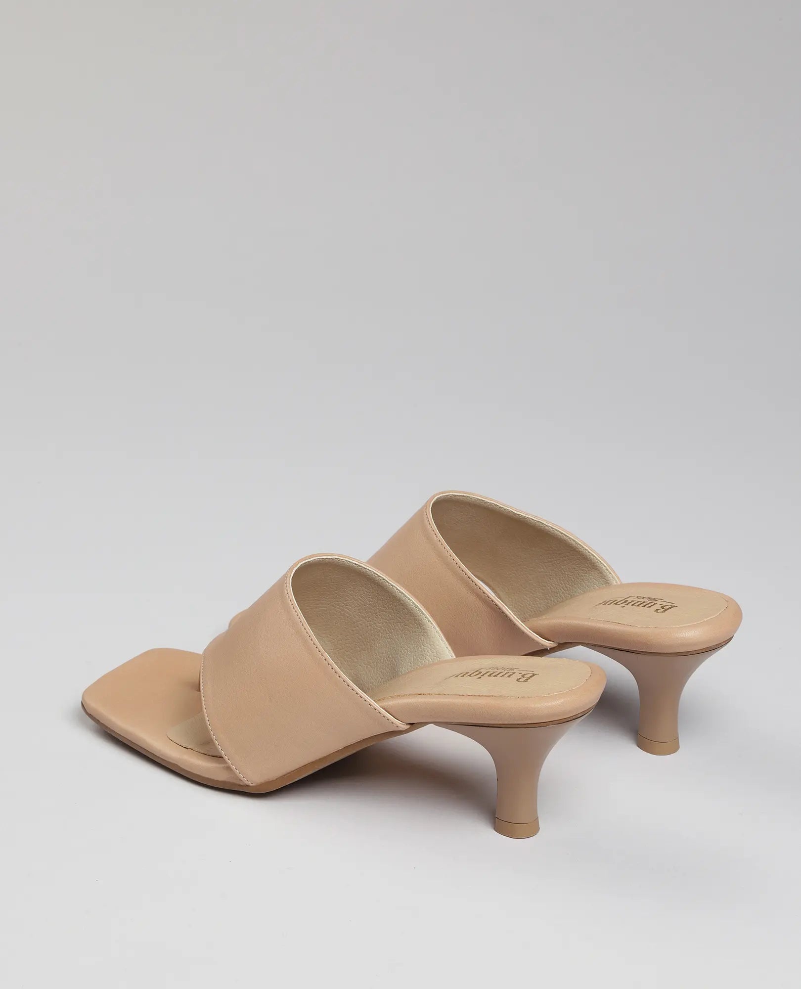 זוג כפכפי אצבע עם עקב בסגנון אמריקאי מבית B.unique בצבע בז', עם רצועות רחבות וקצה מרובע, על רקע אפור בהיר.