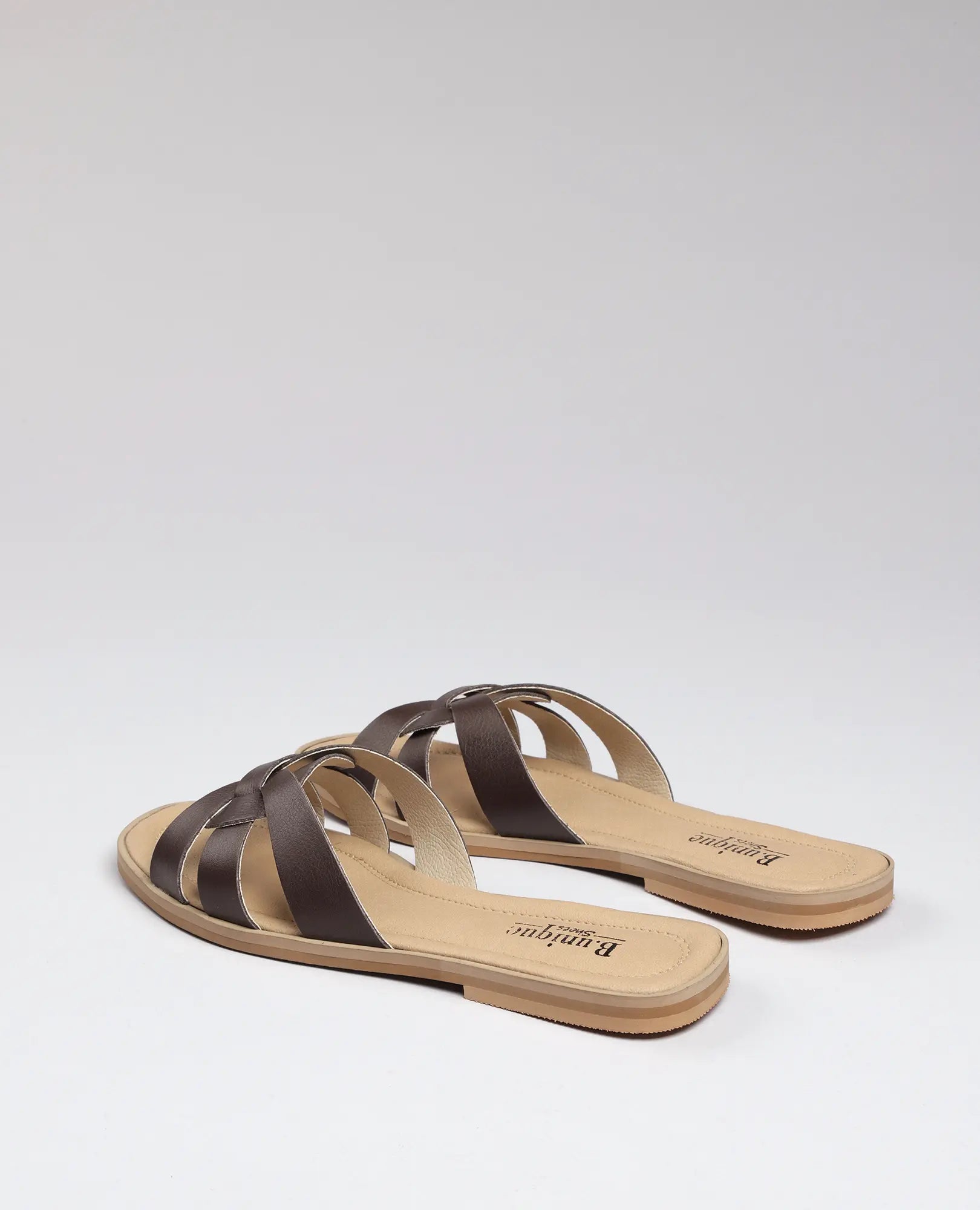 כפכפי רצועות - ריבר לנשים מעור חום מבית B.unique עם רצועות מצטלבות, על רקע אפור בהיר.