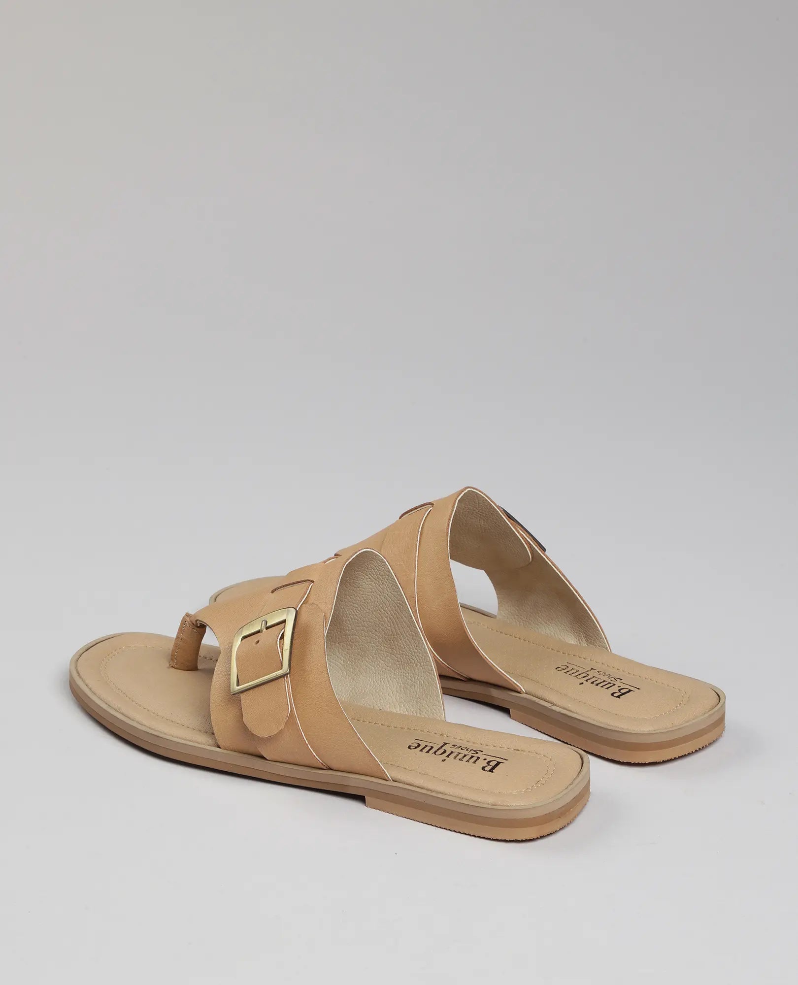 כפכפי אצבע עם אבזם "לורל" מבית B.unique, בעיצוב שטוח בצבע טאן ואבזמי זהב, מוצגים על רקע אפור בהיר.