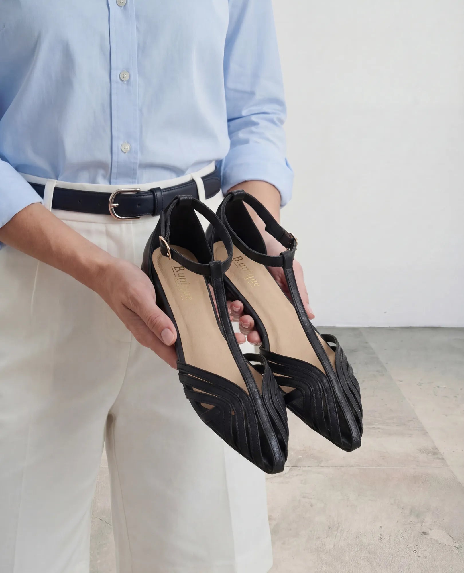 אדם בחולצה תכלת ומכנסיים לבנים מחזיק סנדל שפיץ- מילנה של B.unique.