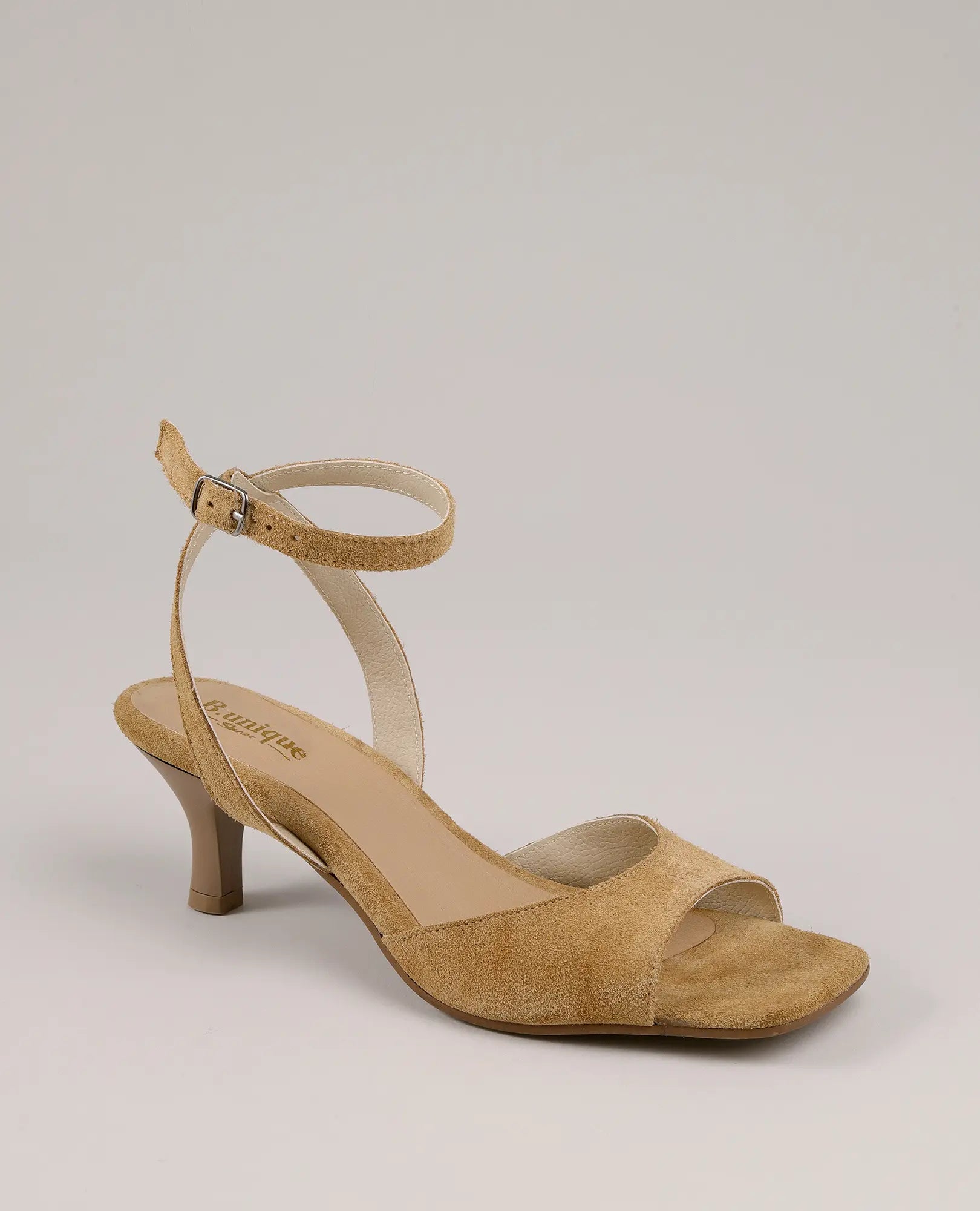 סנדלי עקב של המותג B.unique מעור זמש עם רצועת קרסול ועקב נמוך, אבזם ברצועה, מוצגים על רקע פשוט.