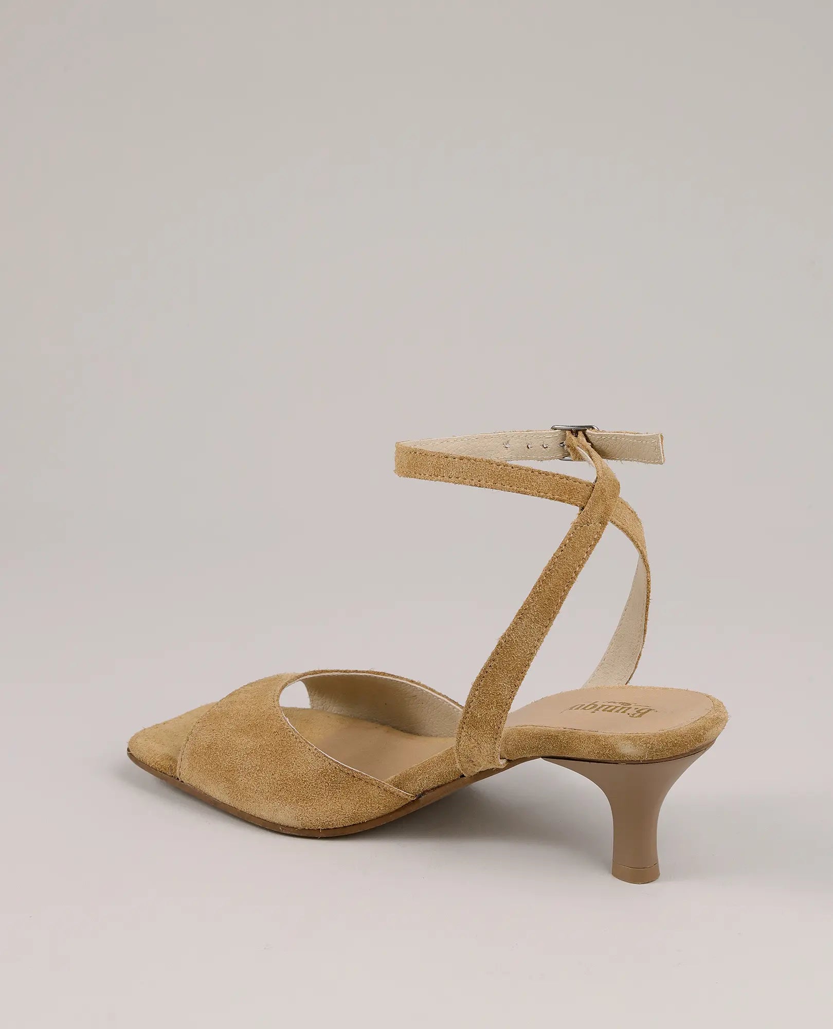 סנדלי עקב של המותג B.unique מעור זמש בגוון טאן, עם רצועת קרסול ועקב נמוך, מוצגים על רקע בהיר.