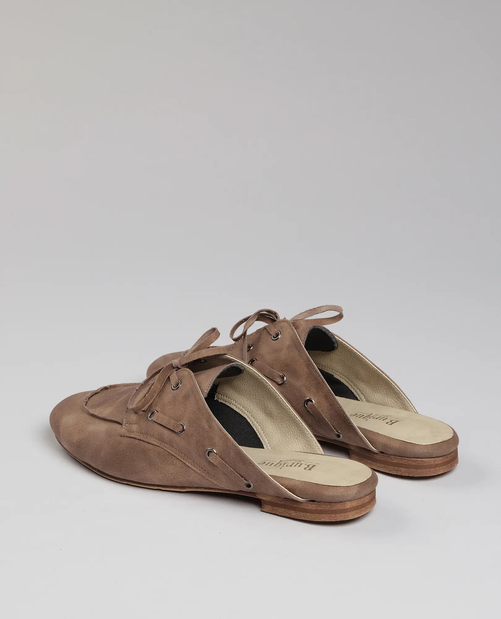 זוג כפכפי מוקסין- לירי חומים מבית B-Unique VEGAN עם שרוכים על רקע אפור בהיר חלק.