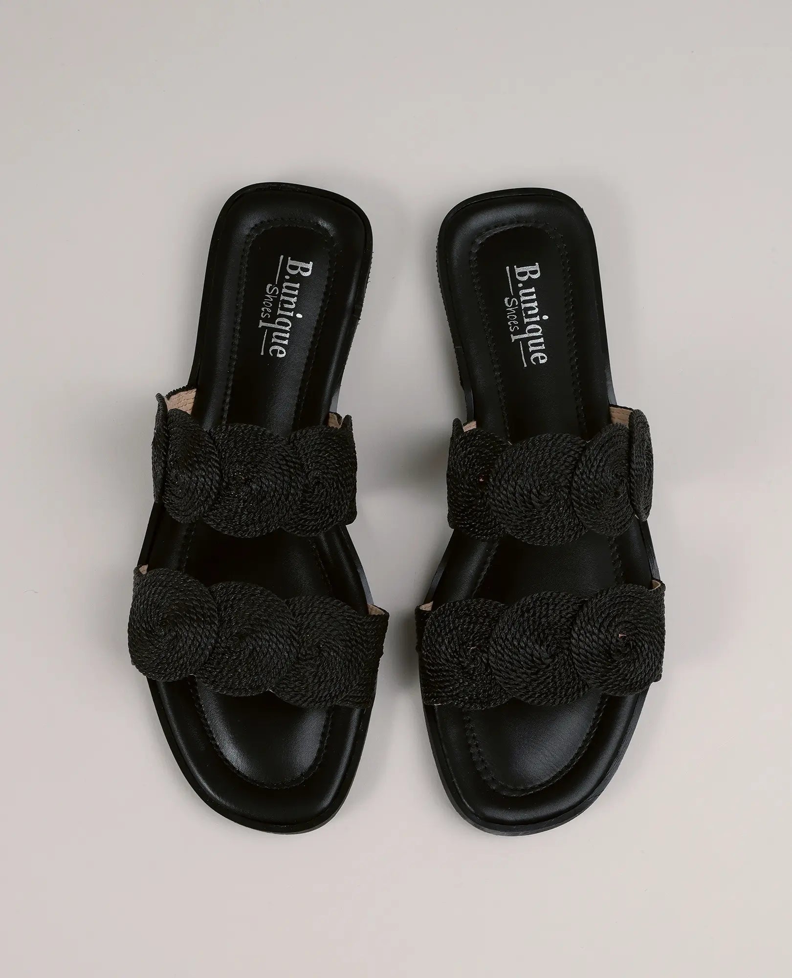 כפכפים עם עיטורי עיגולים - דגם "אלישה" של B-Unique VEGAN, בעיצוב שחור עם שתי רצועות קלועות, מוצגים על רקע בהיר.