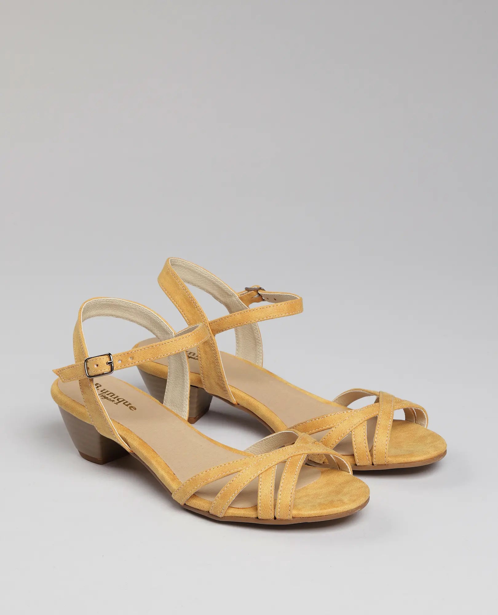 זוג סנדלי עקב-טיילי של B-Unique VEGAN בצבע צהוב, עם רצועות דקות ועקבים נמוכים מעץ על רקע חלק.