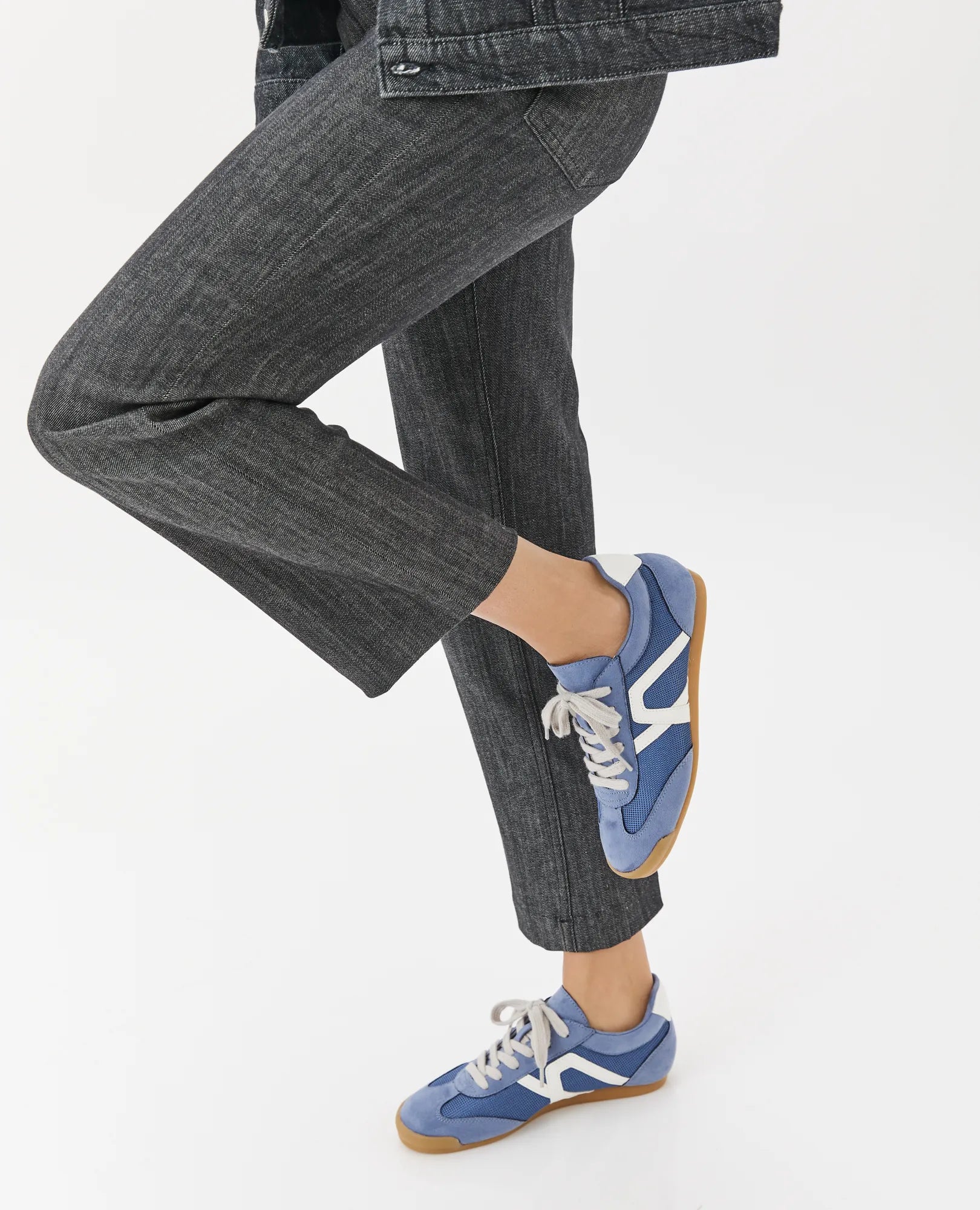 אדם לבוש בג'ינס כהה ונעלי סניקרס מעוצבות – גבריאל מבית B-Unique VEGAN, רגל אחת כפופה, על רקע לבן.
