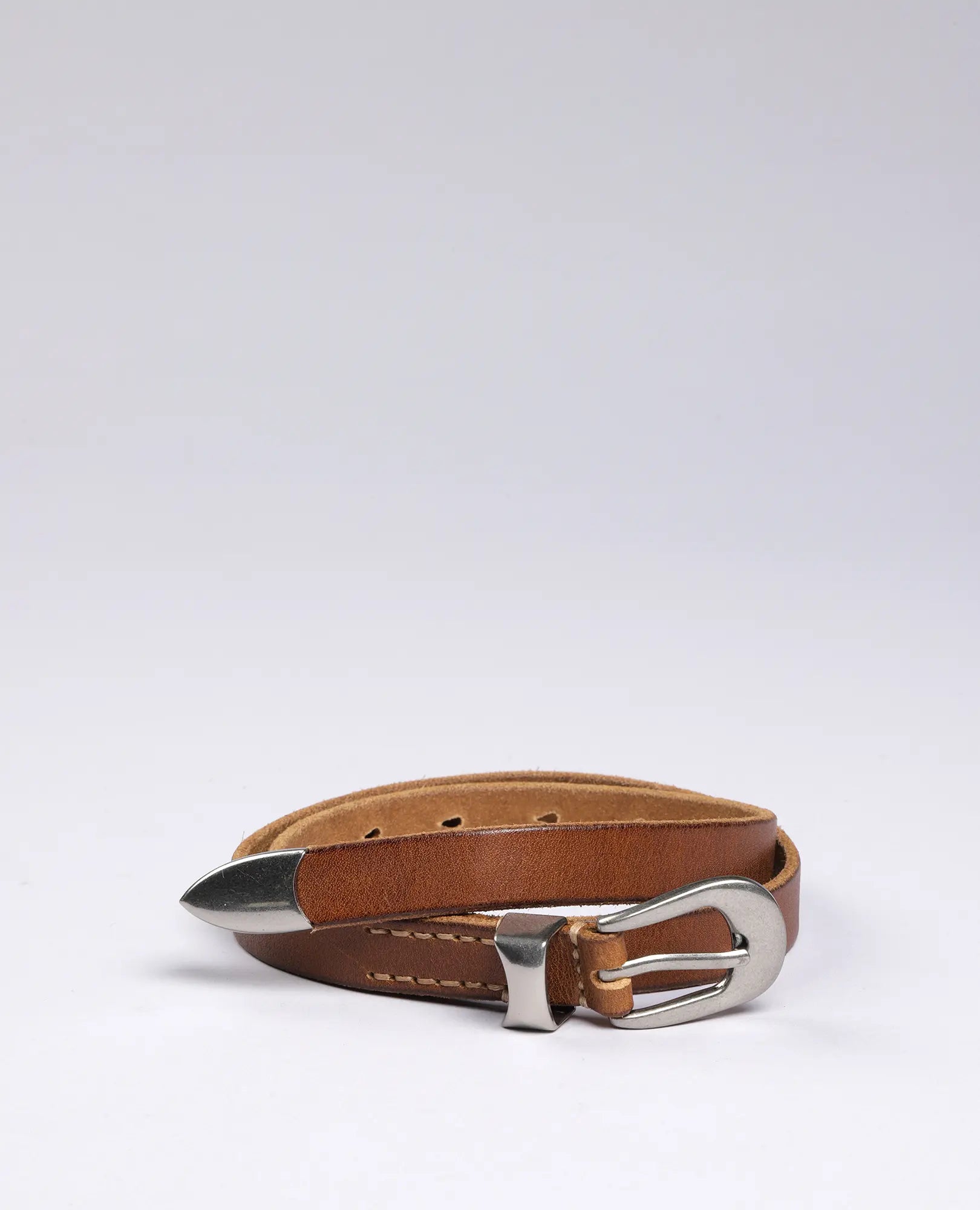 חגורת עור צרה עם אבזם כסף של B Unique, מונחת מגולגלת על רקע בהיר.