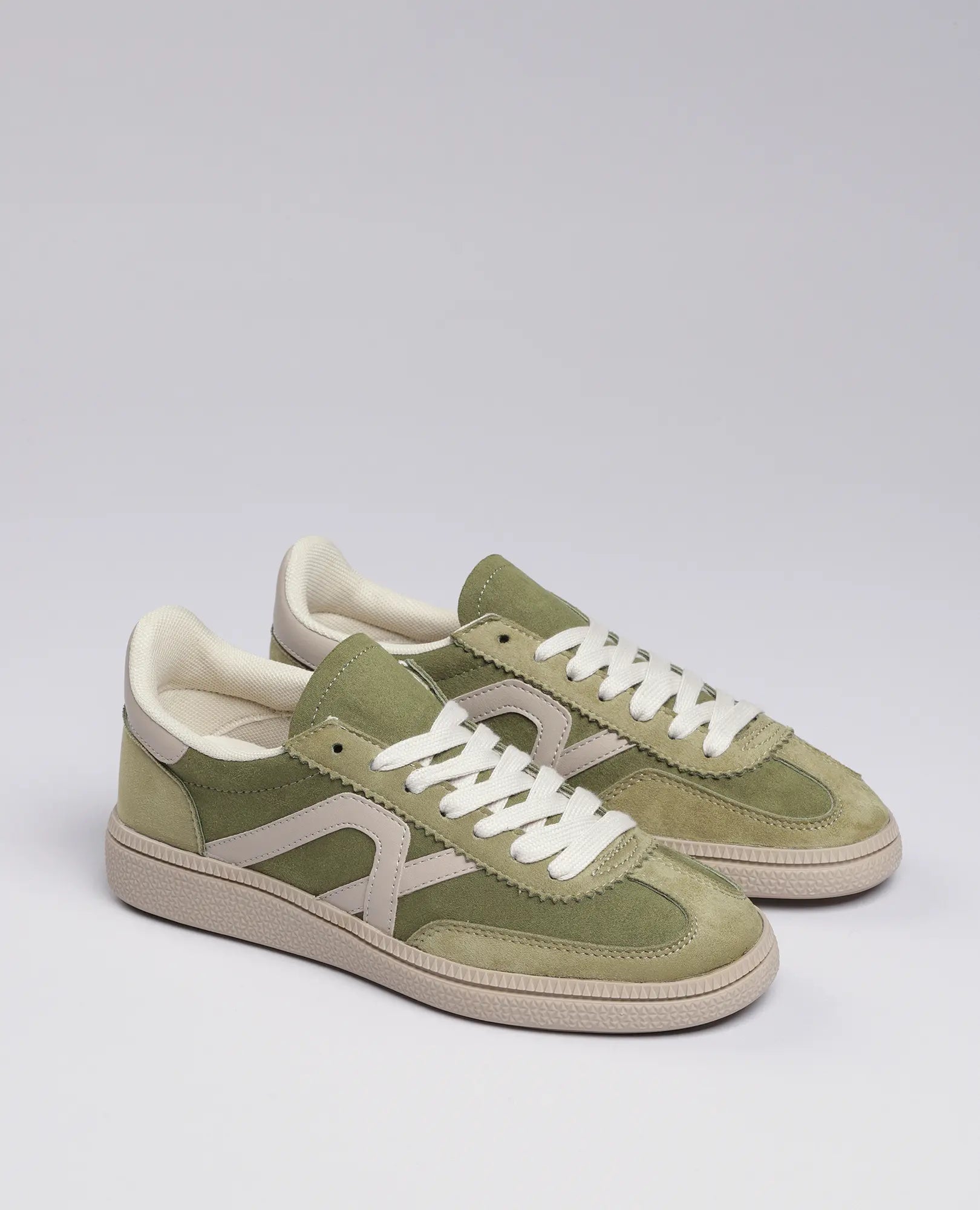 זוג נעלי סניקרס B-Unique VEGAN דמוי זמש- נווה בצבע ירוק ובז' עם שרוכים לבנים על רקע אפור בהיר.