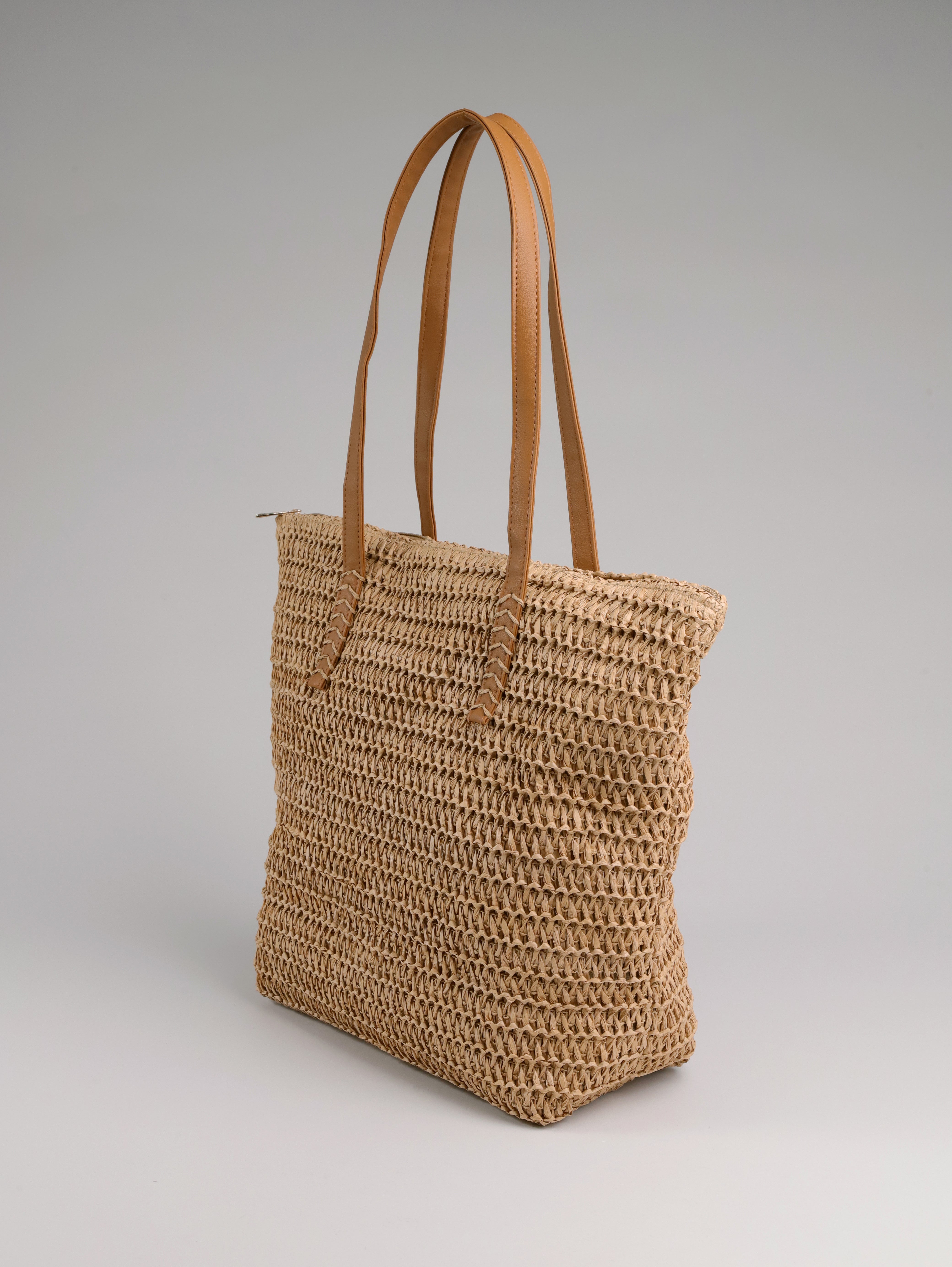 תיק קש של B-Unique Bags עם שתי ידיות עור חומות, בעיצוב ייחודי על רקע אפור בהיר.