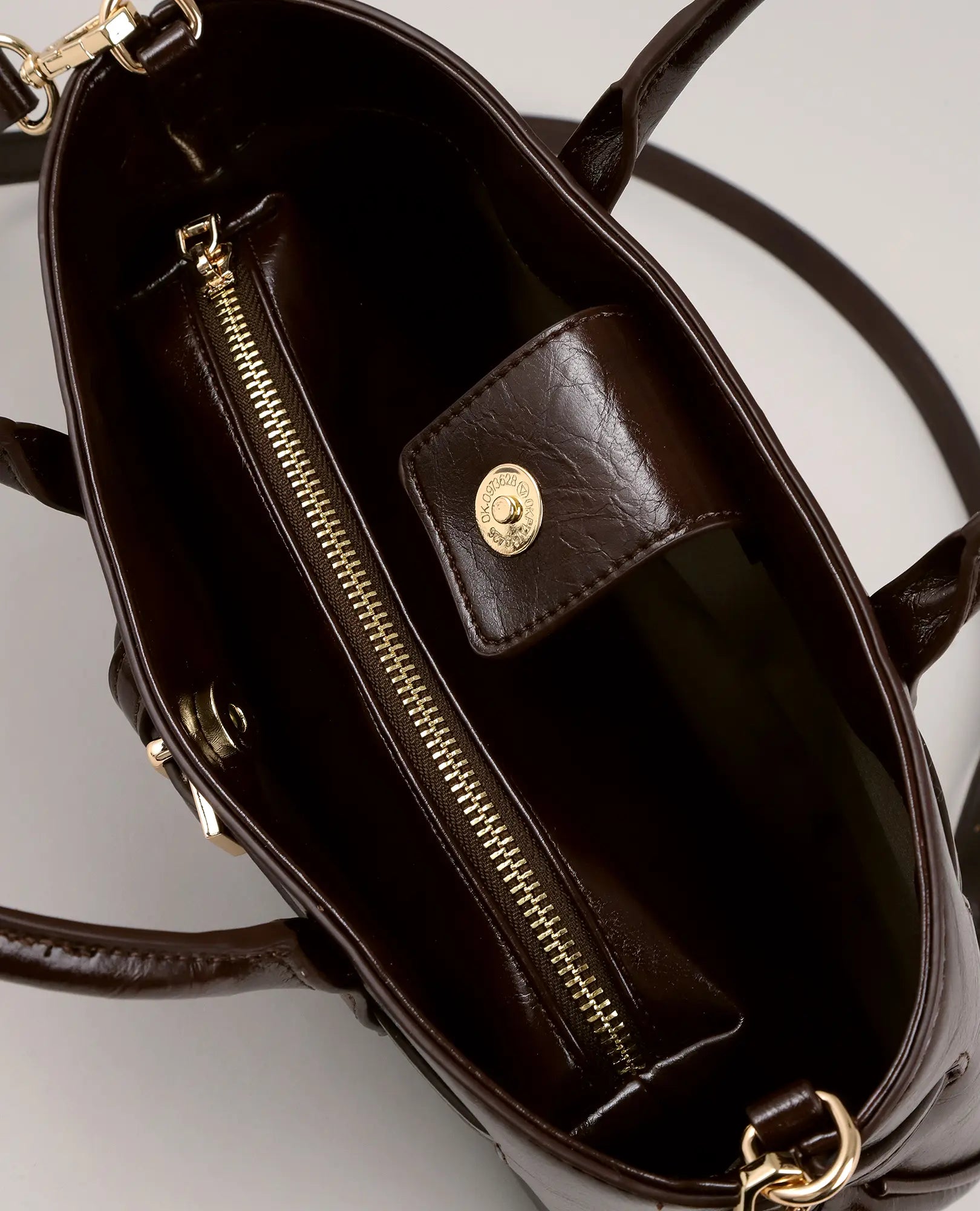 תיק צד בצבע חום כהה של המותג B-Unique Bags עם רוכסן זהוב, תא עם סגירת לחצן ורצועת כתף גלויה.
