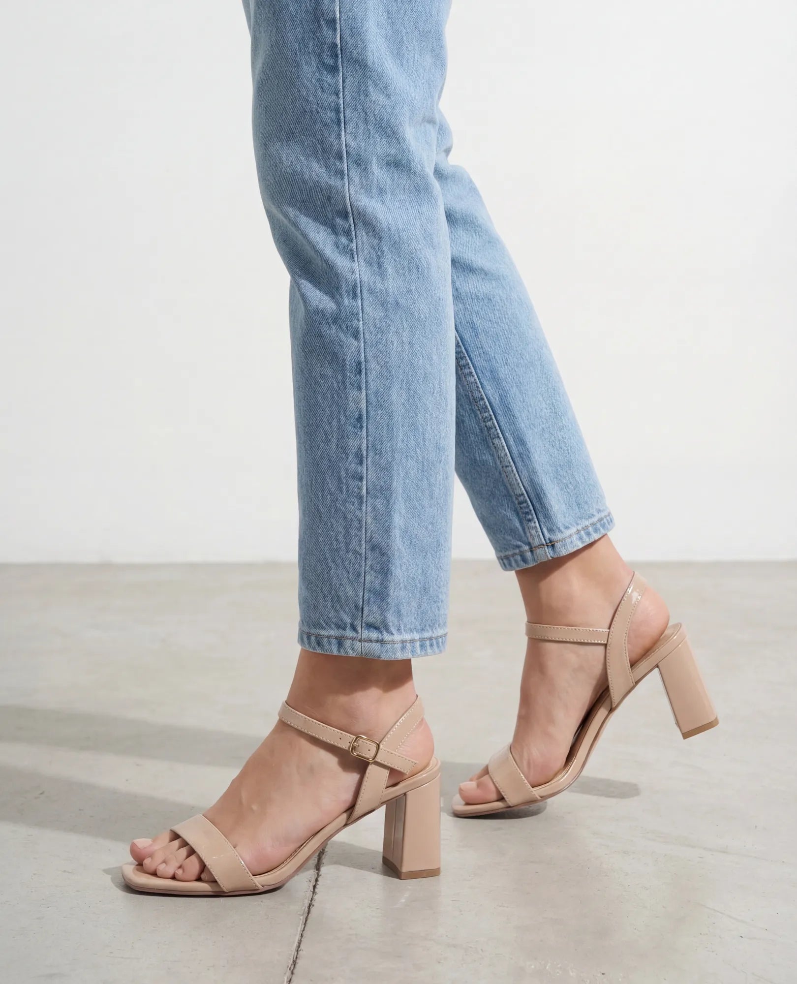 אדם לבוש בג'ינס תכלת ובסנדלי עקב B-Unique VEGAN – אפריל בטאופ, עומד על רצפה חלקה ובהירה.