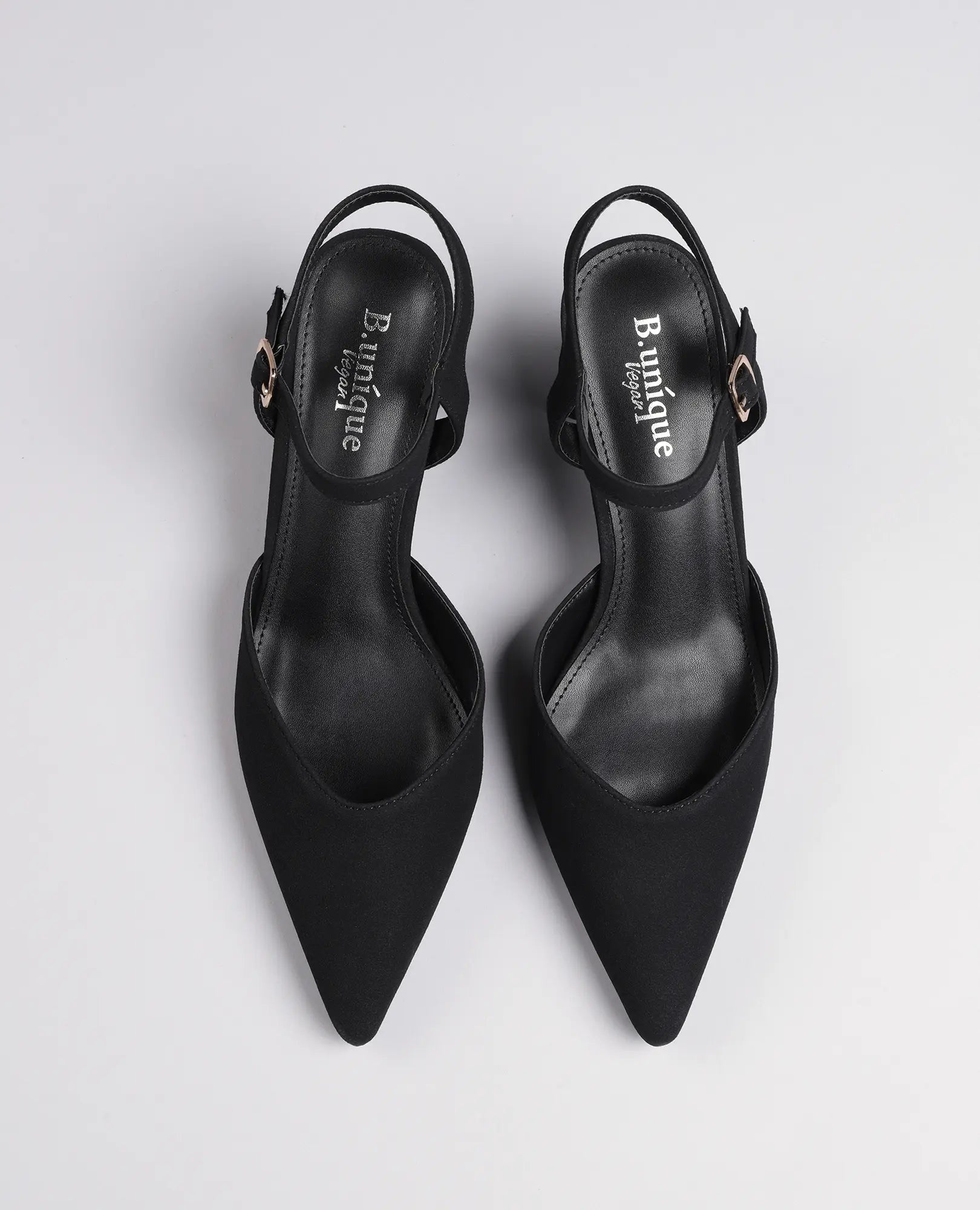 זוג נעלי עקב - "ארין" מבית B-Unique VEGAN, נעלי סלינגבק שחורות עם קצה מחודד, בעלות מראה דמוי זמש ורצועות בקרסול על רקע לבן.