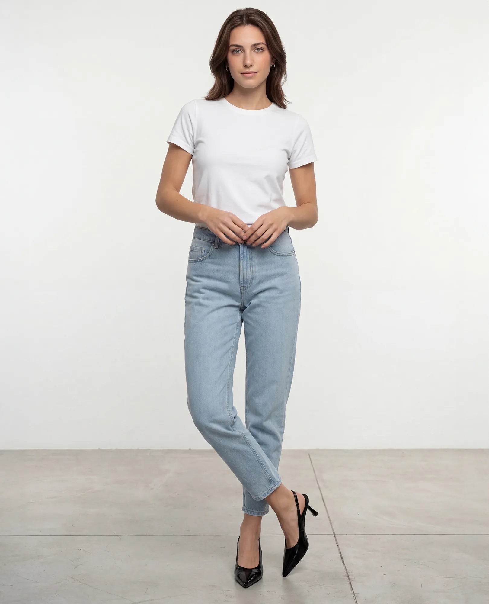 אישה בחולצת טריקו לבנה, ג'ינס תכלת ונעלי עקב שפיץ של B-Unique VEGAN, דורון, מצטלמת ברגליים משוכלות על רקע בהיר.