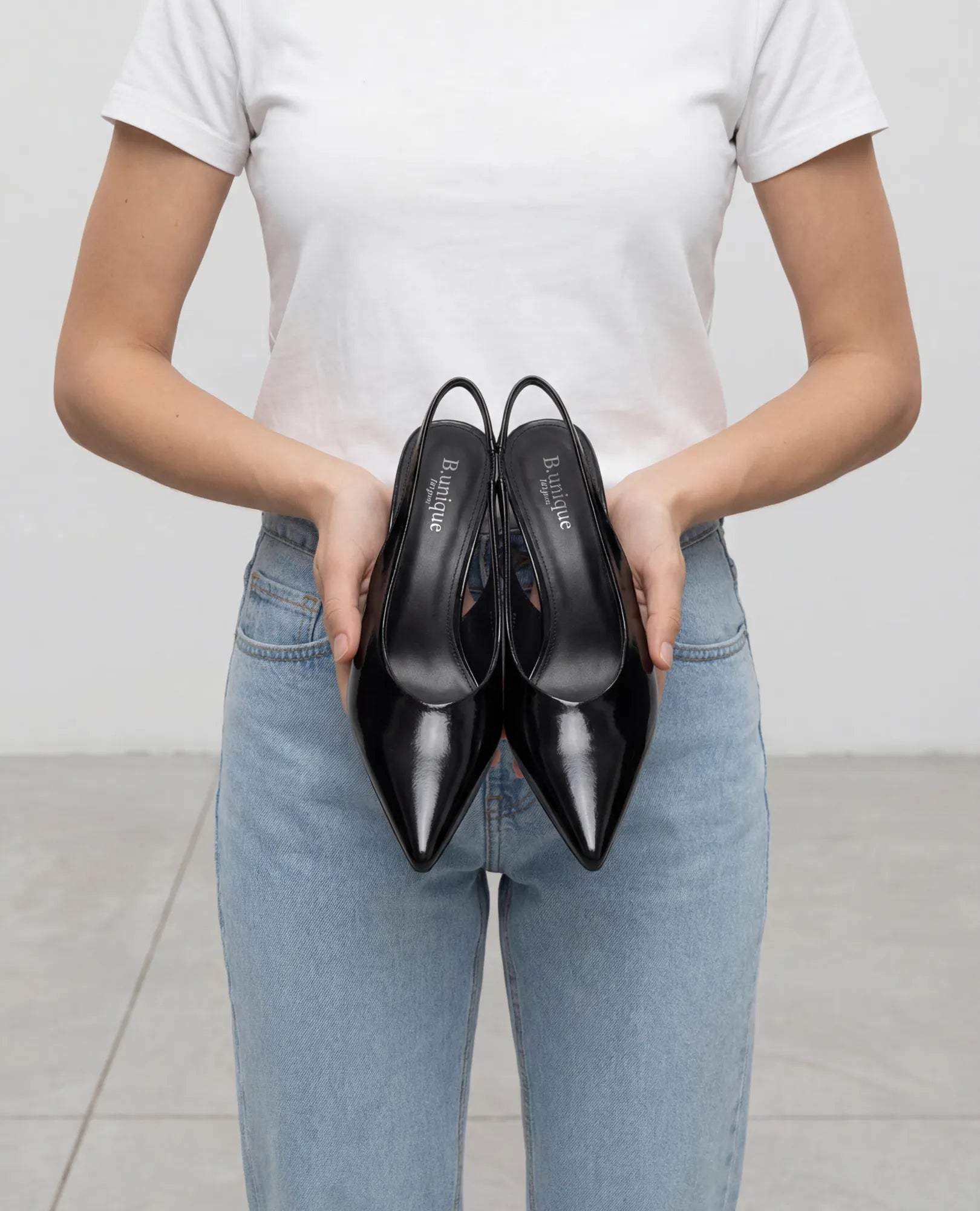 אדם לבוש בג'ינס וחולצה לבנה מחזיק B-Unique VEGAN נעלי עקב שפיץ- דורון עם עקב בינוני.