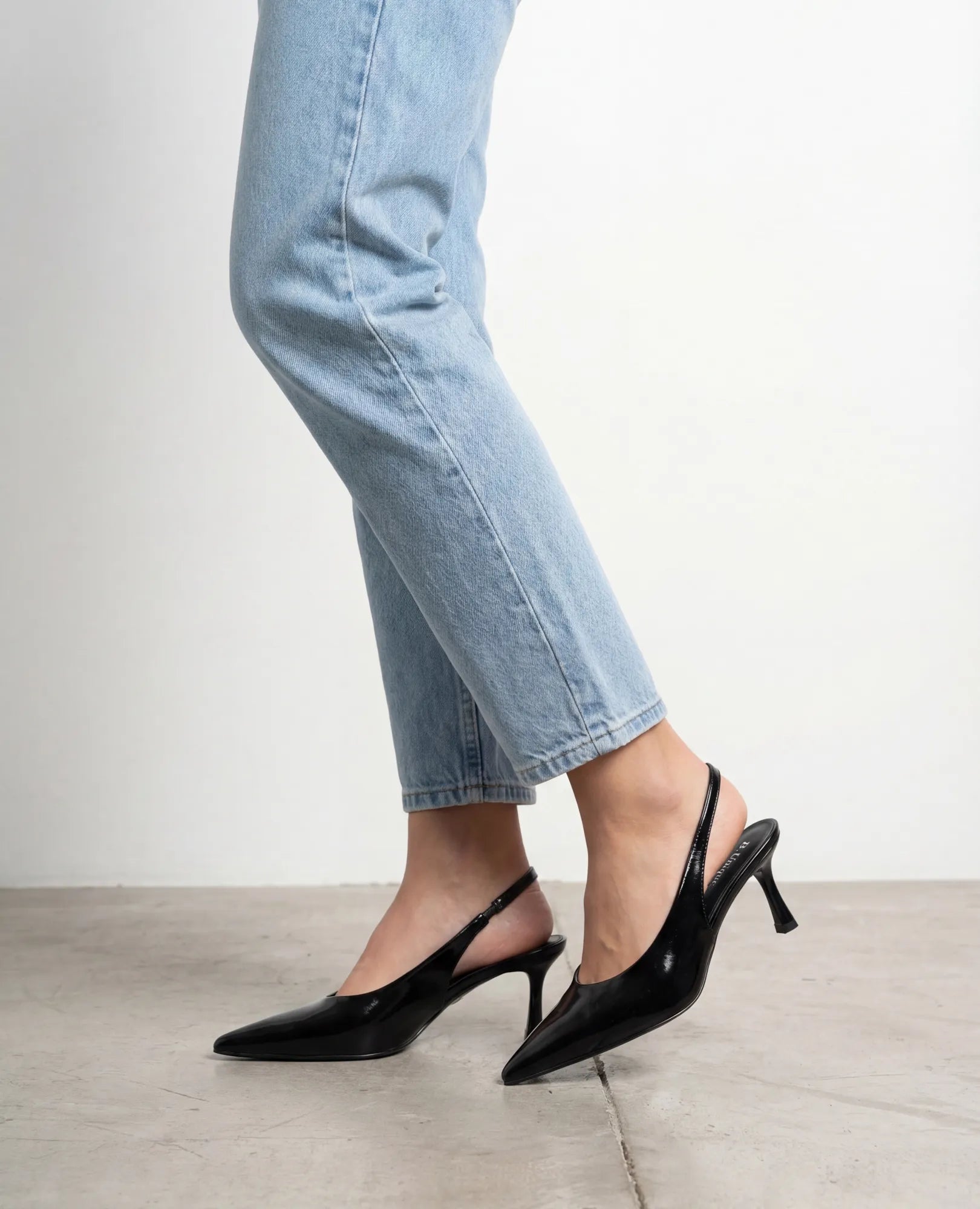 אדם לבוש בג'ינס תכלת ונעלי עקב שפיץ- דורון מבית B-Unique VEGAN על רצפה בהירה על רקע לבן.