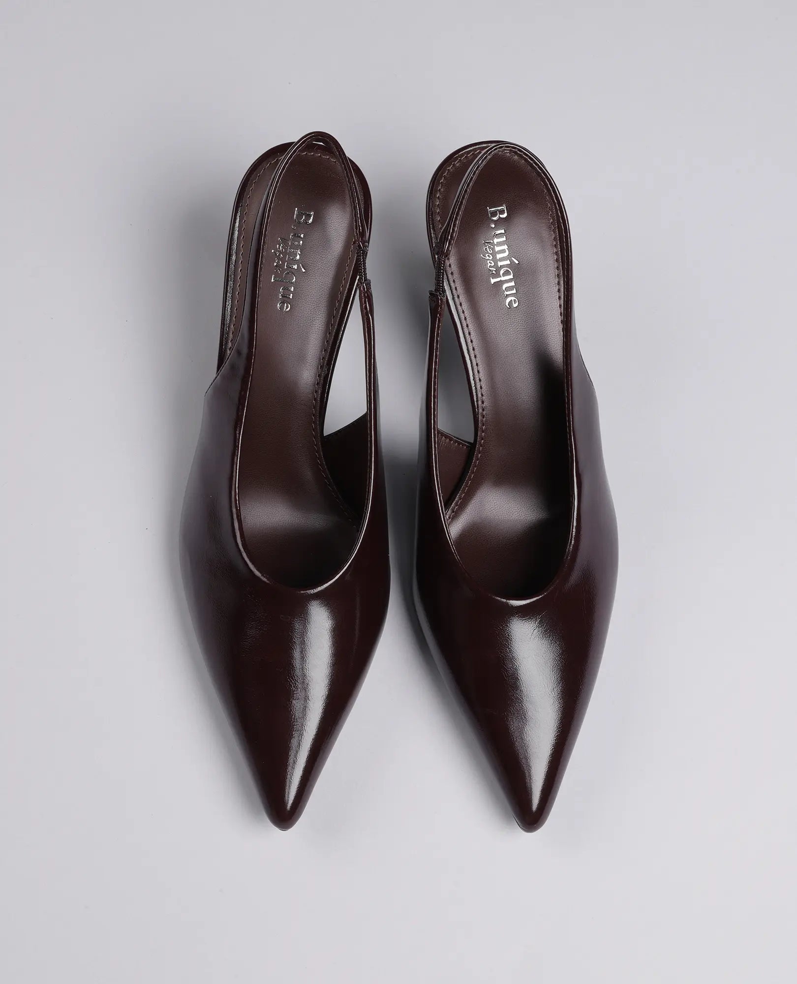 זוג נעלי עקב שפיץ- דורון מבית B-Unique VEGAN עם עקב בינוני בצבע חום כהה על רקע אפור בהיר.