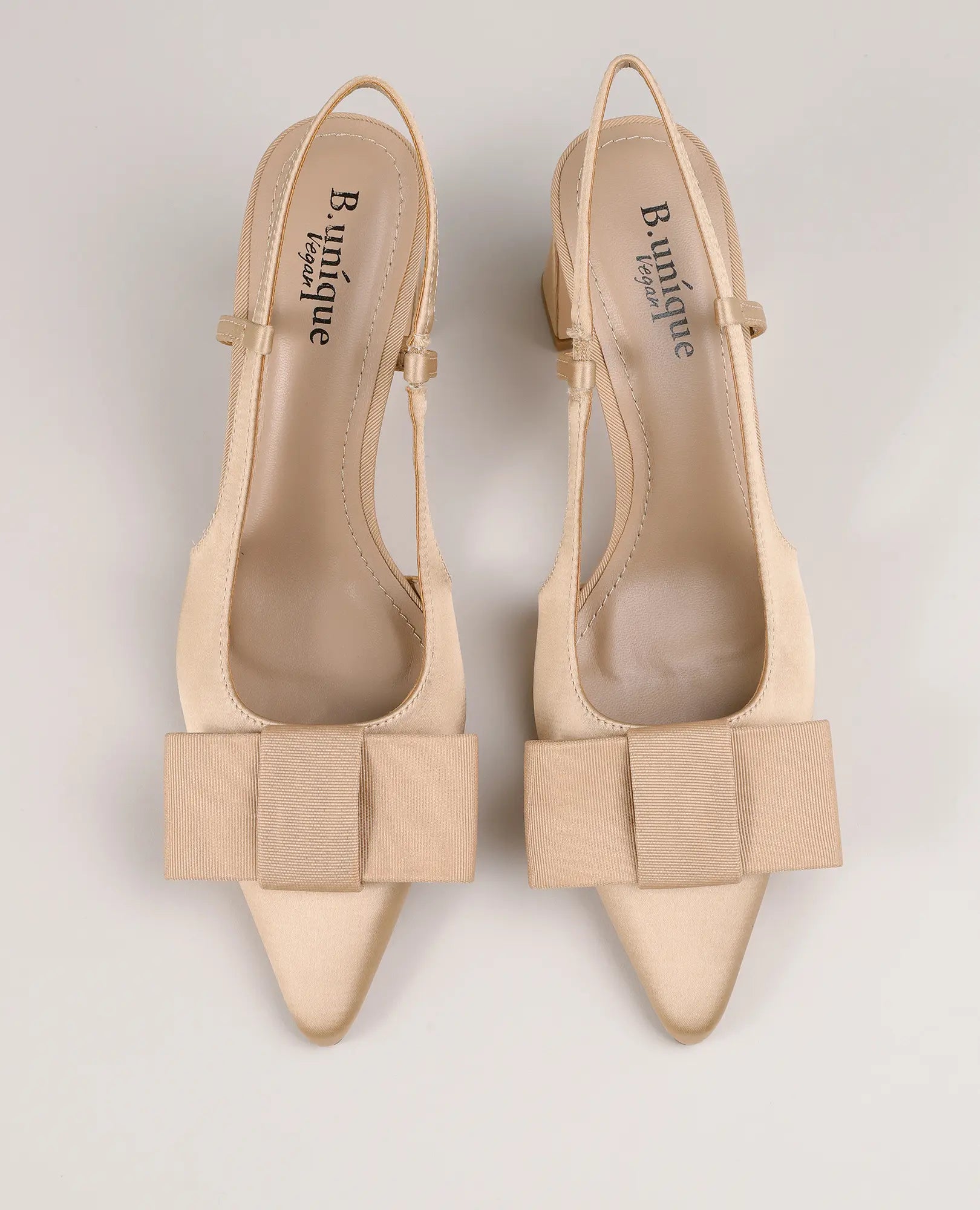 B-Unique VEGAN – סנדלי עקב עם פפיון בגוון בז', עם פפיון גדול, ועיצוב עליון על רקע בהיר.