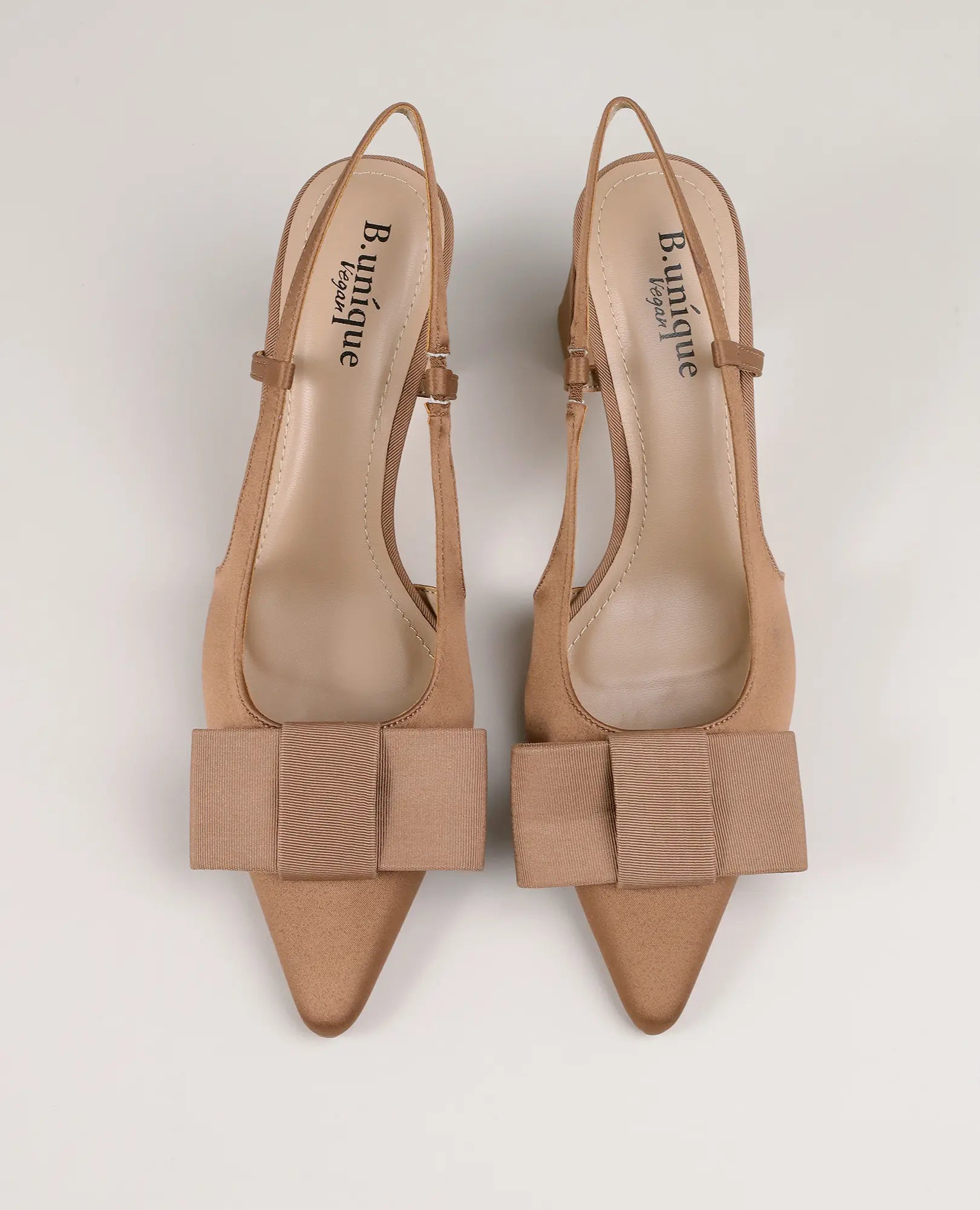 B-Unique VEGAN – סנדלי עקב עם פפיונים בגוון חום בהיר, עם פפיונים גדולים, מצולמים מלמעלה על רקע בהיר.