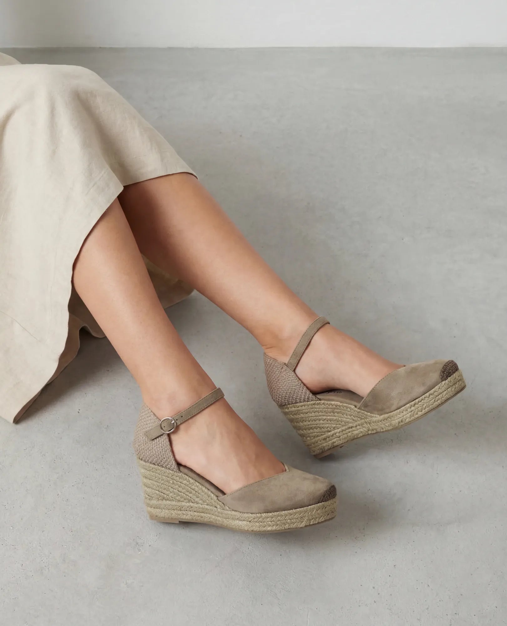 אישה בנעלי פלטפורמה מדגם "כרם" של B-Unique VEGAN עם רצועת קרסול וחצאית בצבע בז', יושבת על בטון.