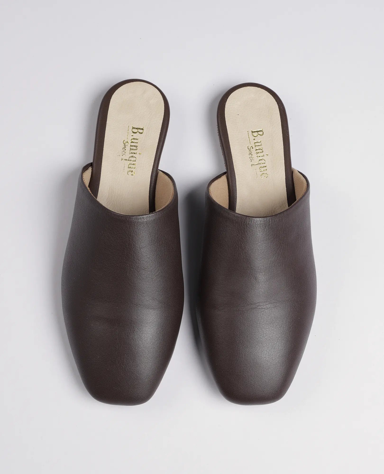 זוג כפכפים שטוחים של B.unique – כפכפי רוקס מעור חום עם רפידות בצבע בז', מונחים זה לצד זה על רקע לבן.