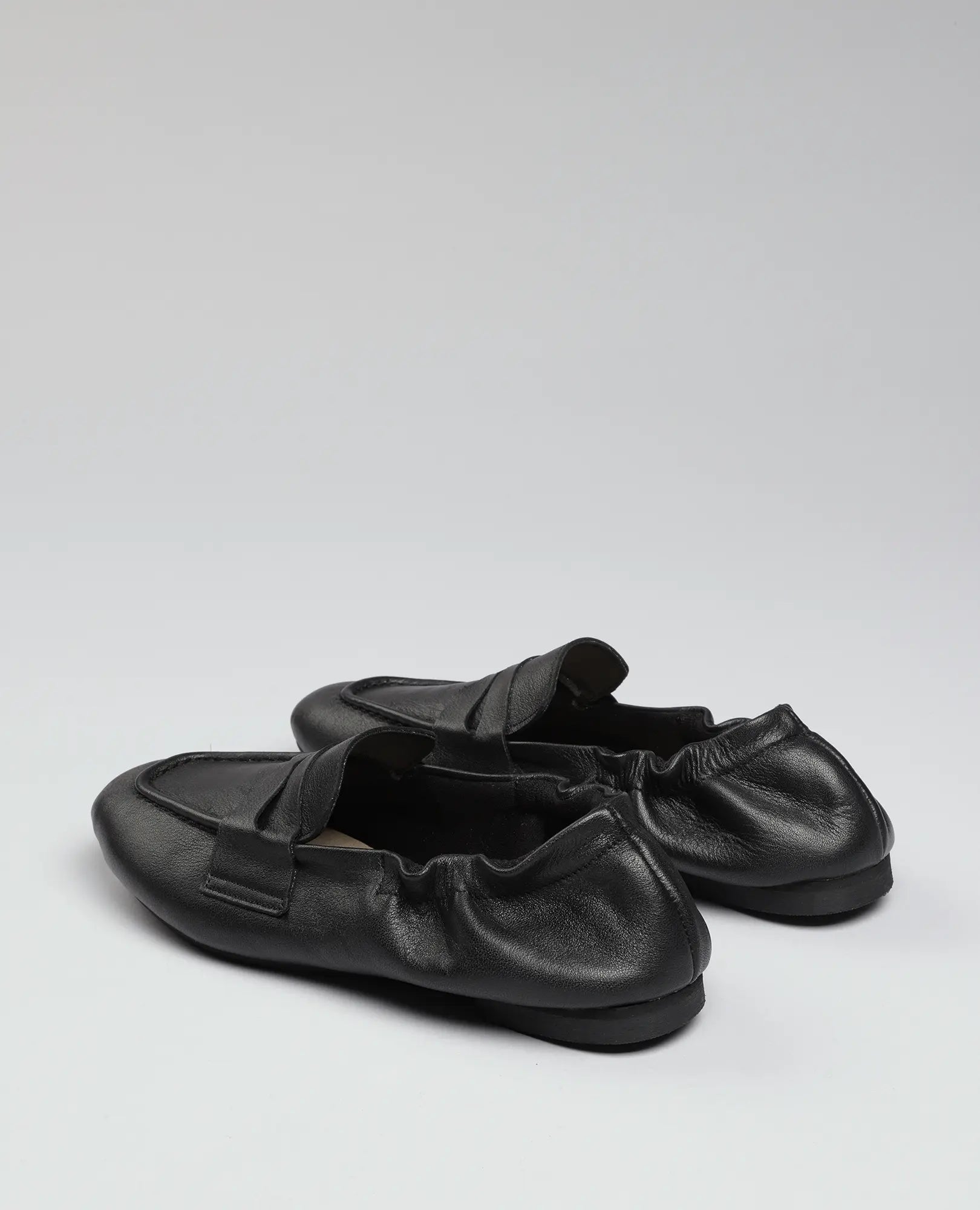 זוג נעלי מוקסין-נוריאל שחורות של B.unique עם גב אלסטי, מוצגות על רקע לבן חלק.