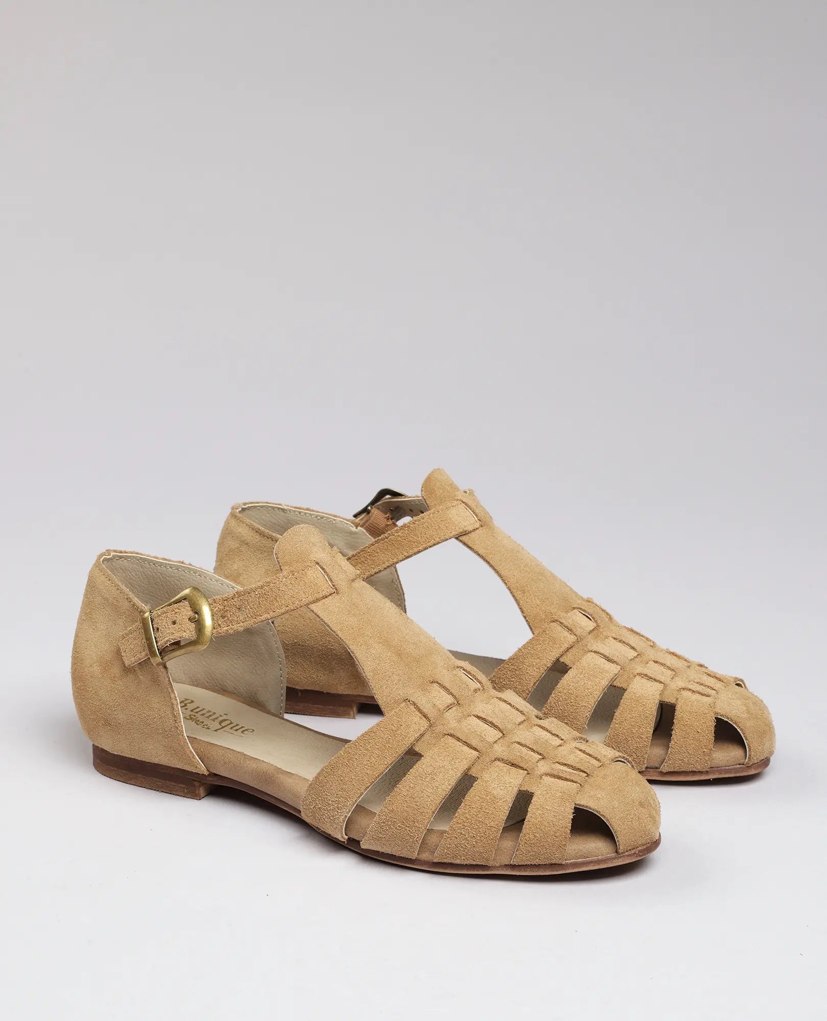 סנדלי רצועות - דגם "קאסי" של B.unique מעור זמש עם רצועת קרסול ועקב נמוך על רקע בהיר.