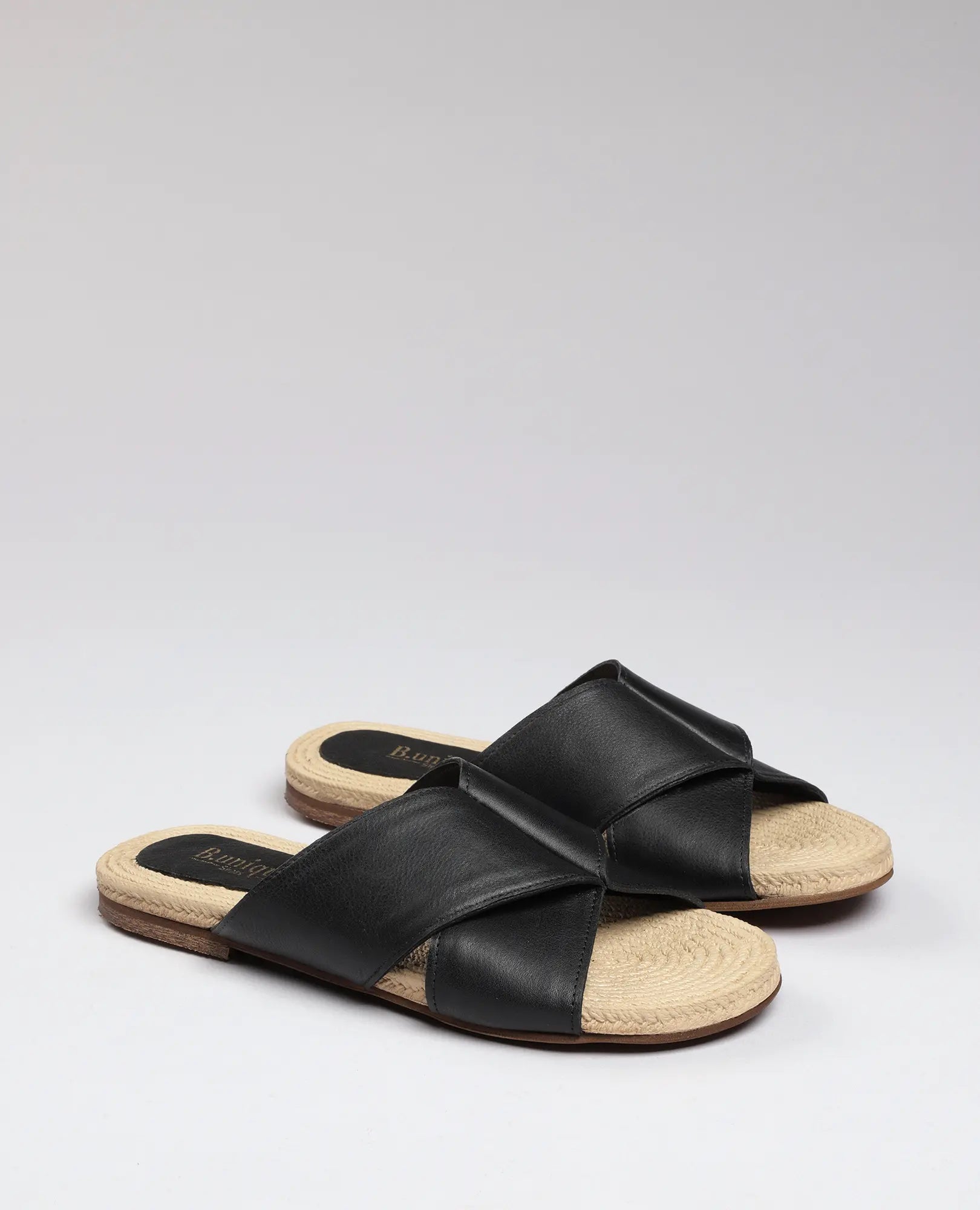 זוג כפכפים שטוחים – דגם "גליה" מבית B.unique, עם סוליות בצבע חום בהיר ורצועות עור שחורות בצורת שתי וערב על רקע חלק.