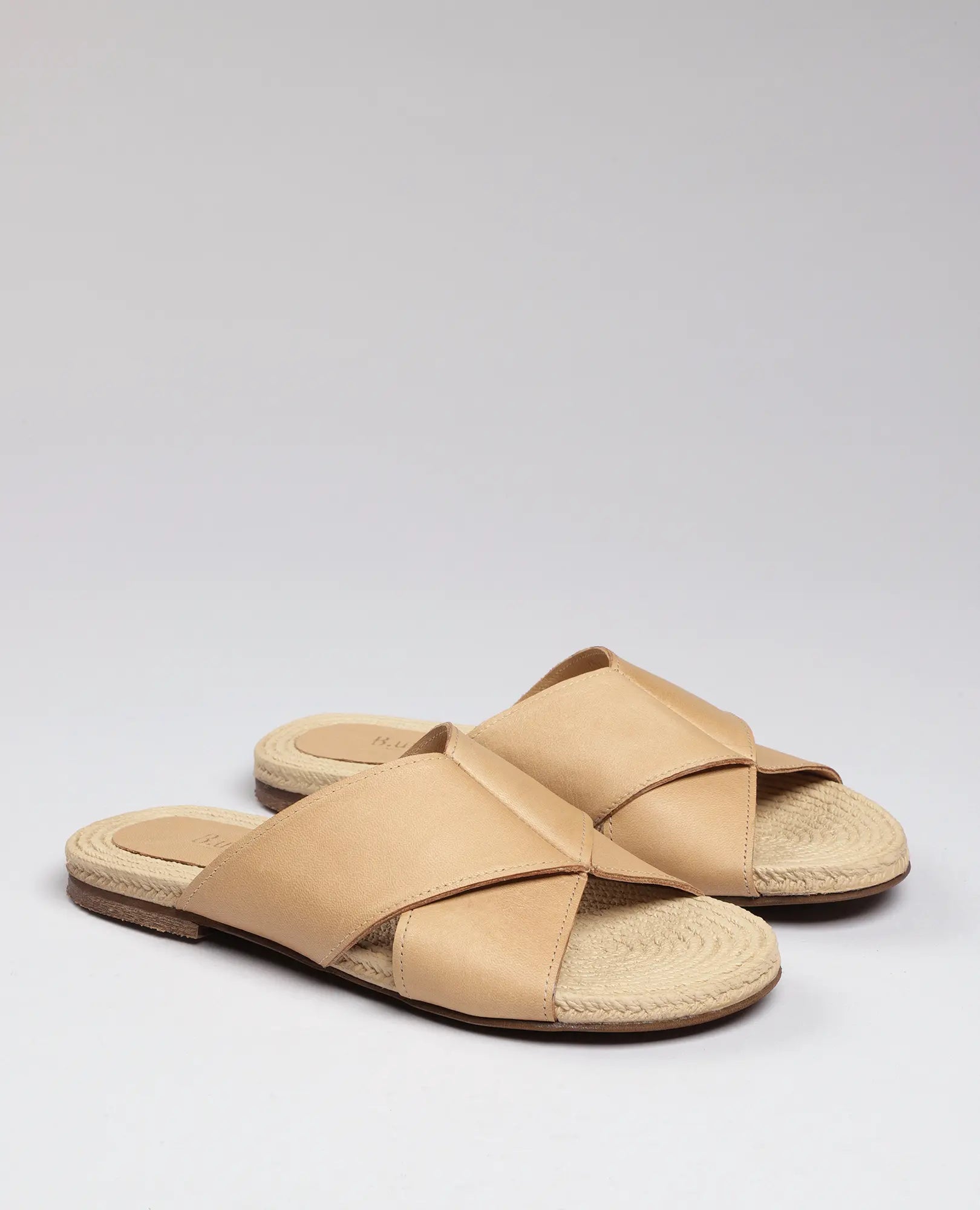 כפכפים שטוחים של B.unique לנשים, עם רצועות עור מצטלבות, מוצגים על רקע בהיר.