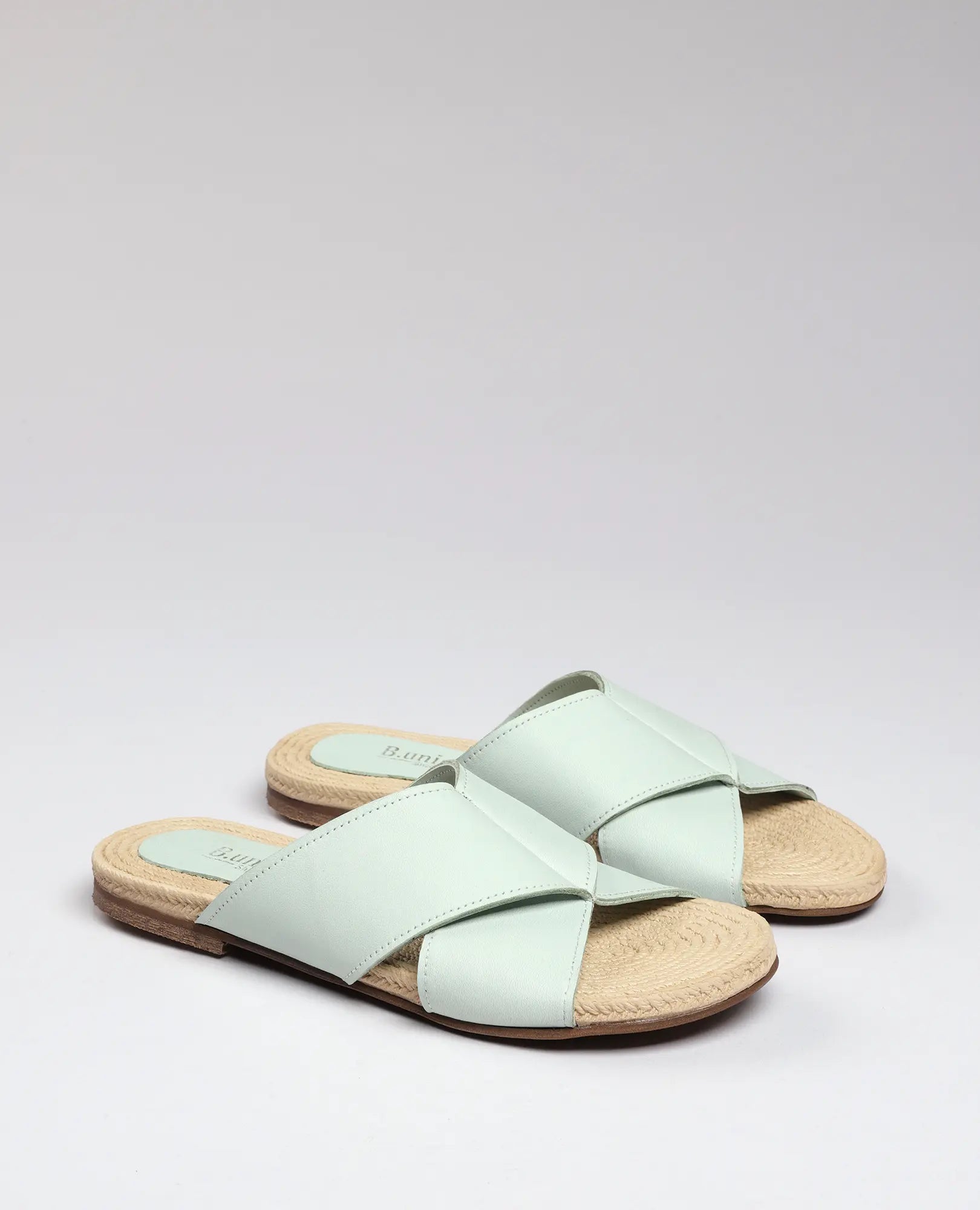 זוג כפכפים שטוחים של B.unique מדגם "גליה" בצבע ירוק בהיר, עם רצועות מצטלבות וסוליות שזורות בצבע בז' על רקע אחיד.