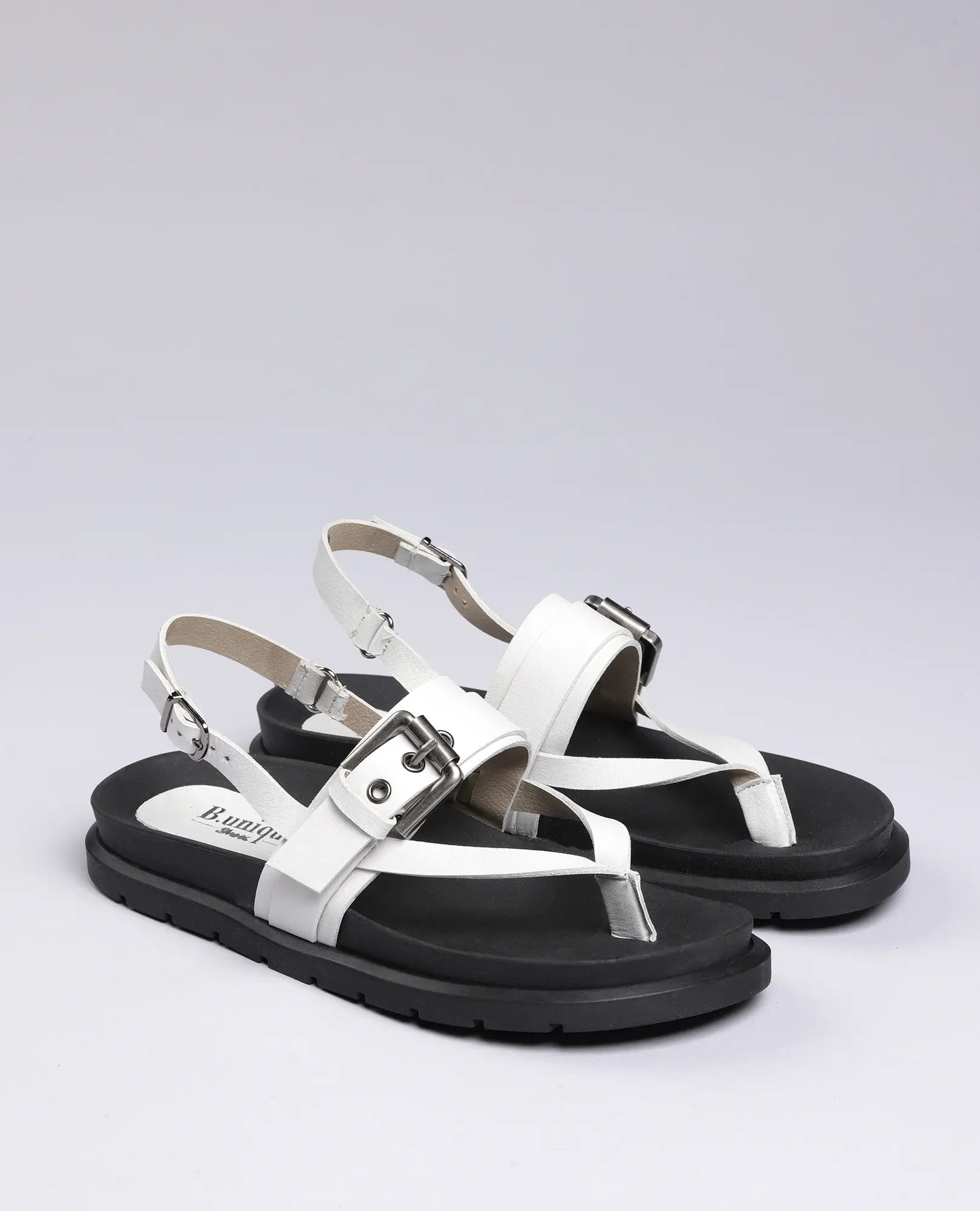 B.unique סנדלי אצבע - פואט: סנדלי עור בשחור ולבן עם רצועות אבזם וסוליות עבות על רקע בהיר.