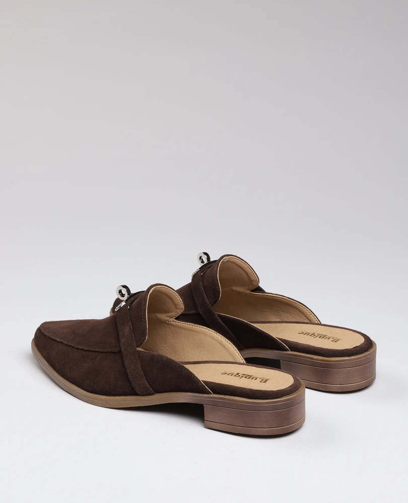 כפכפי מוקסין-ניקי של B.unique, עשויים עור זמש חום עם עקב עץ נמוך, מוצגים מהצד האחורי.