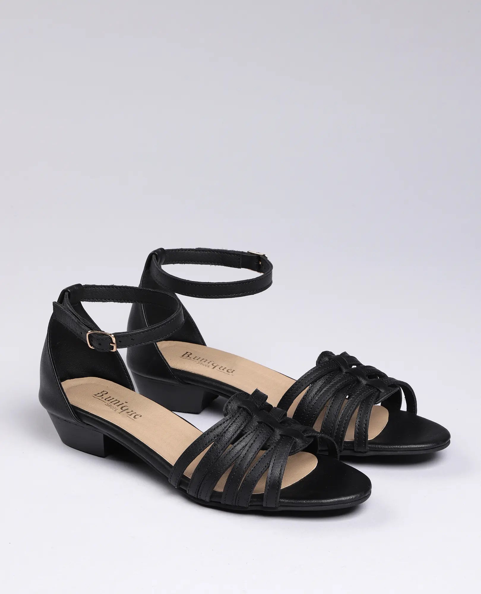 סנדלי רצועות דקות של B.unique לנשים, עם רצועות עור שחורות ועקב נמוך, מוצגים על רקע בהיר.