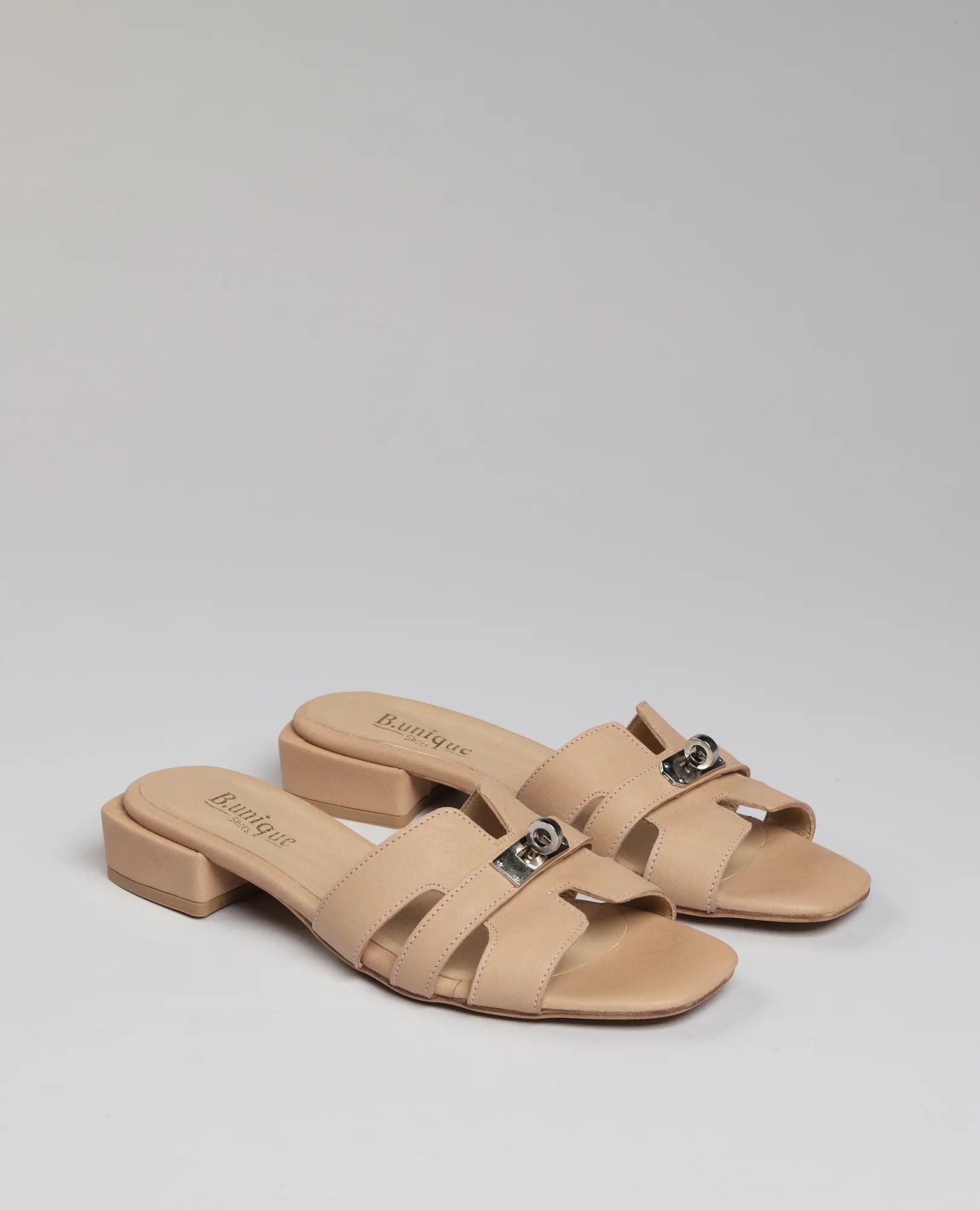 כפכפי רצועות עם אבזם – נעה מבית B.unique: כפכפי עור בצבע בז', רצועות רחבות, עקב נמוך ואבזמי מתכת.