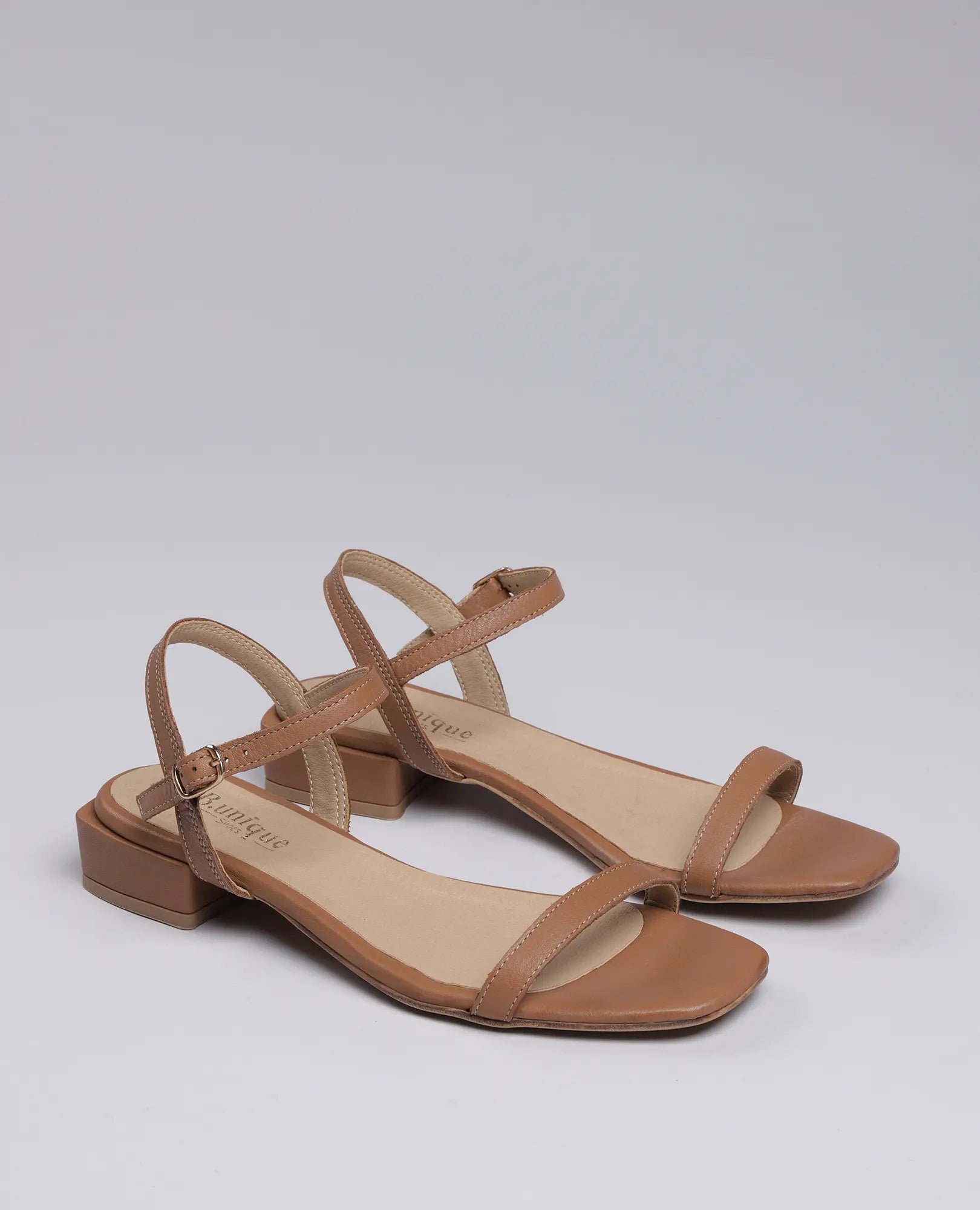 זוג סנדלי רצועות-ווילו של B.unique בצבע קאמל, עם רצועות בקרסול ואצבעות פתוחות על רקע בהיר וחלק.
